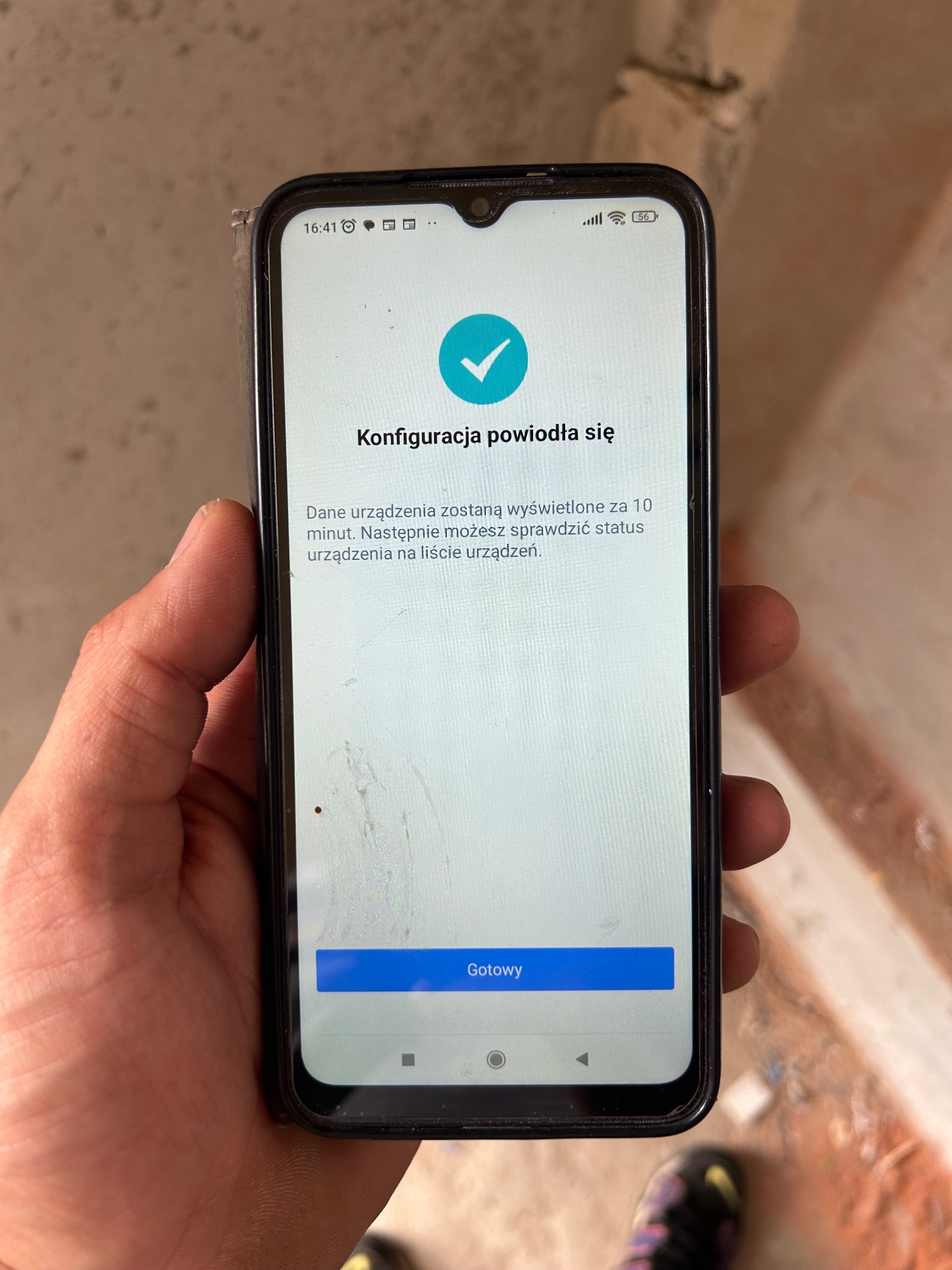 Ekran smartfona w dłoni z komunikatem o pomyślnej konfiguracji. Widoczny stan sieci 5G. Tło to surowa ściana w trakcie prac wykończeniowych.