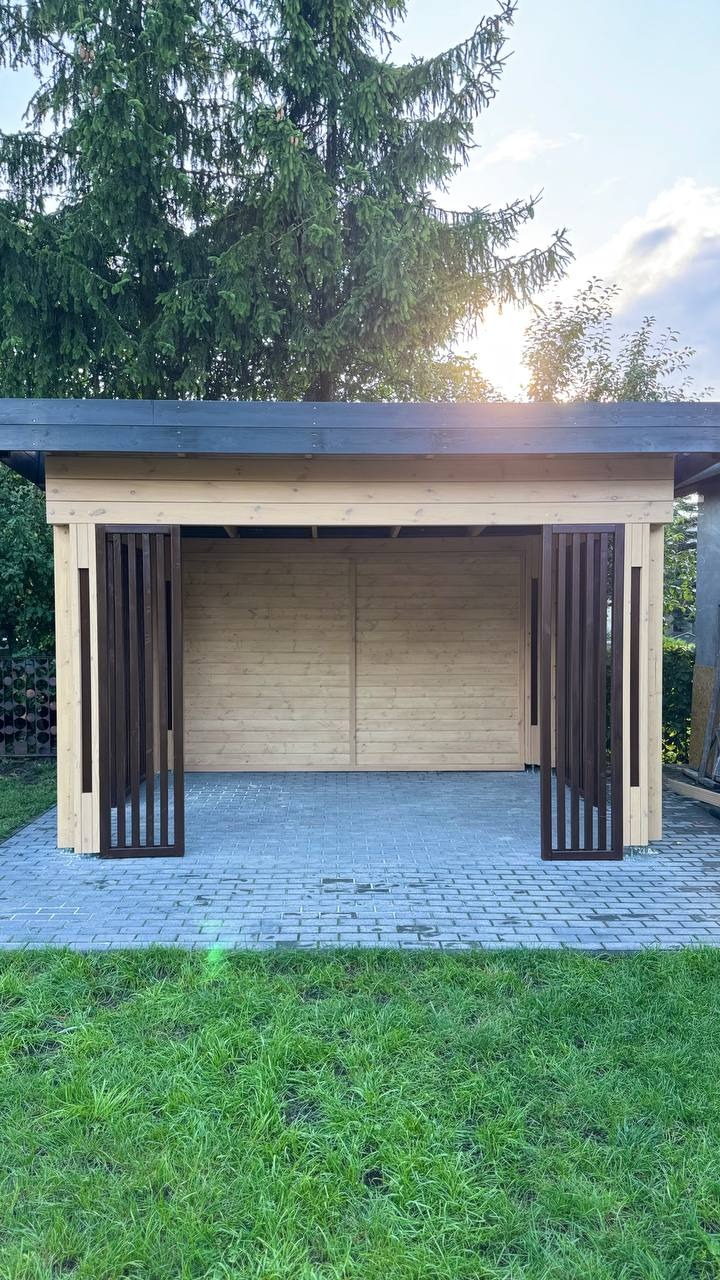 Drewniana altana z przesuwnymi panelami, jasne drewno, ciemny dach, kostka brukowa i trawnik. Ujęcie z przodu, widoczne detale konstrukcyjne.