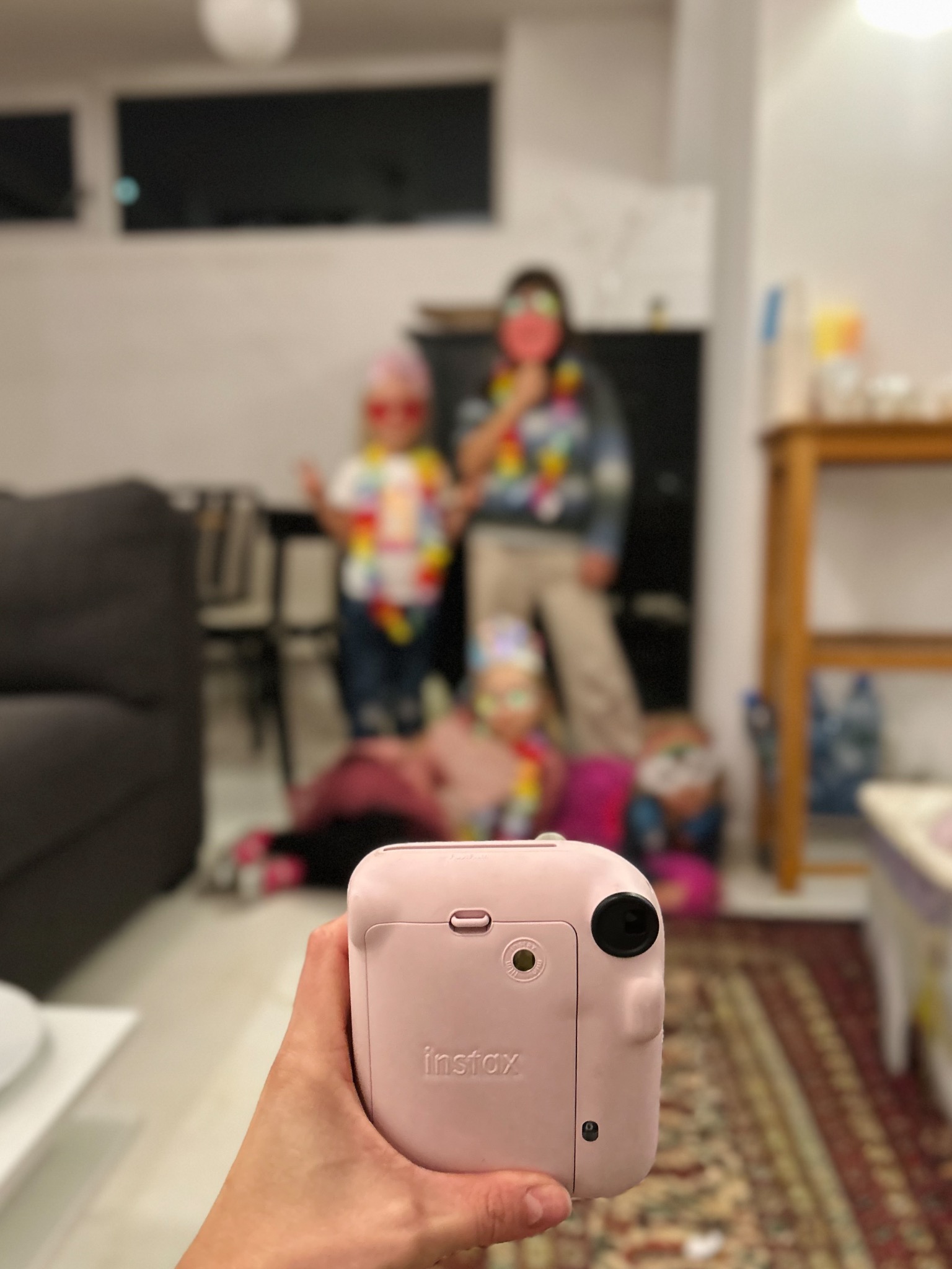 Różowy aparat Instax w dłoni, w tle rozmazane dzieci w przebraniach, Konstancin-Jeziorna. Pamiątkowe zdjęcie z imprezy urodzinowej.