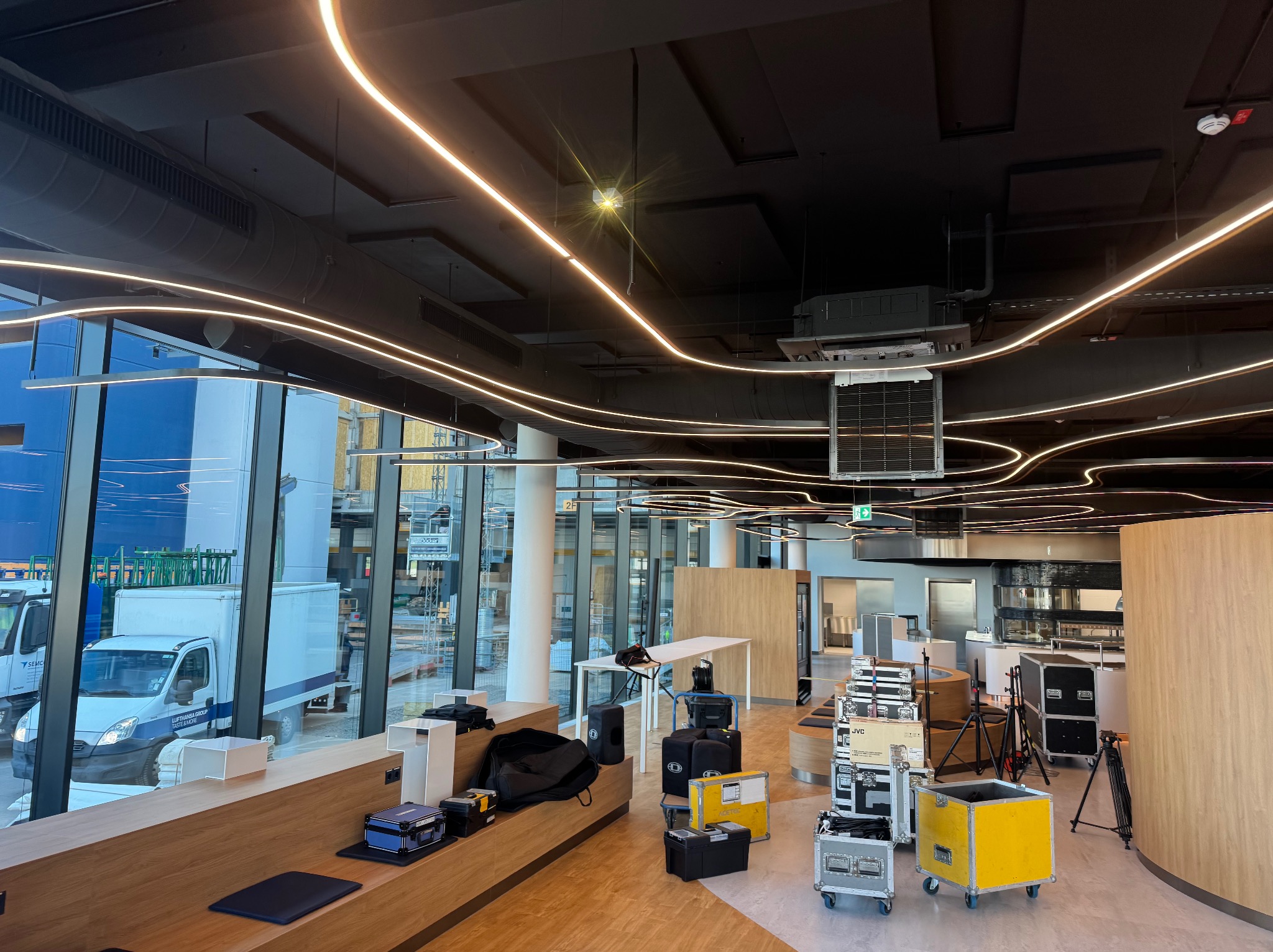 Nowoczesne oświetlenie LED w biurze z czarnym sufitem i widokiem na zewnątrz przez duże okna. Sprzęt audio i oświetleniowy na podłodze.