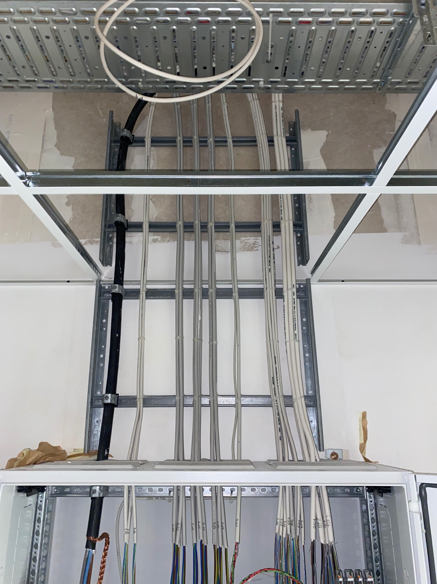 Rozprowadzenie kabli elektrycznych w metalowych korytkach pod sufitem podwieszanym, widoczna skrzynka rozdzielcza z podłączonymi przewodami.