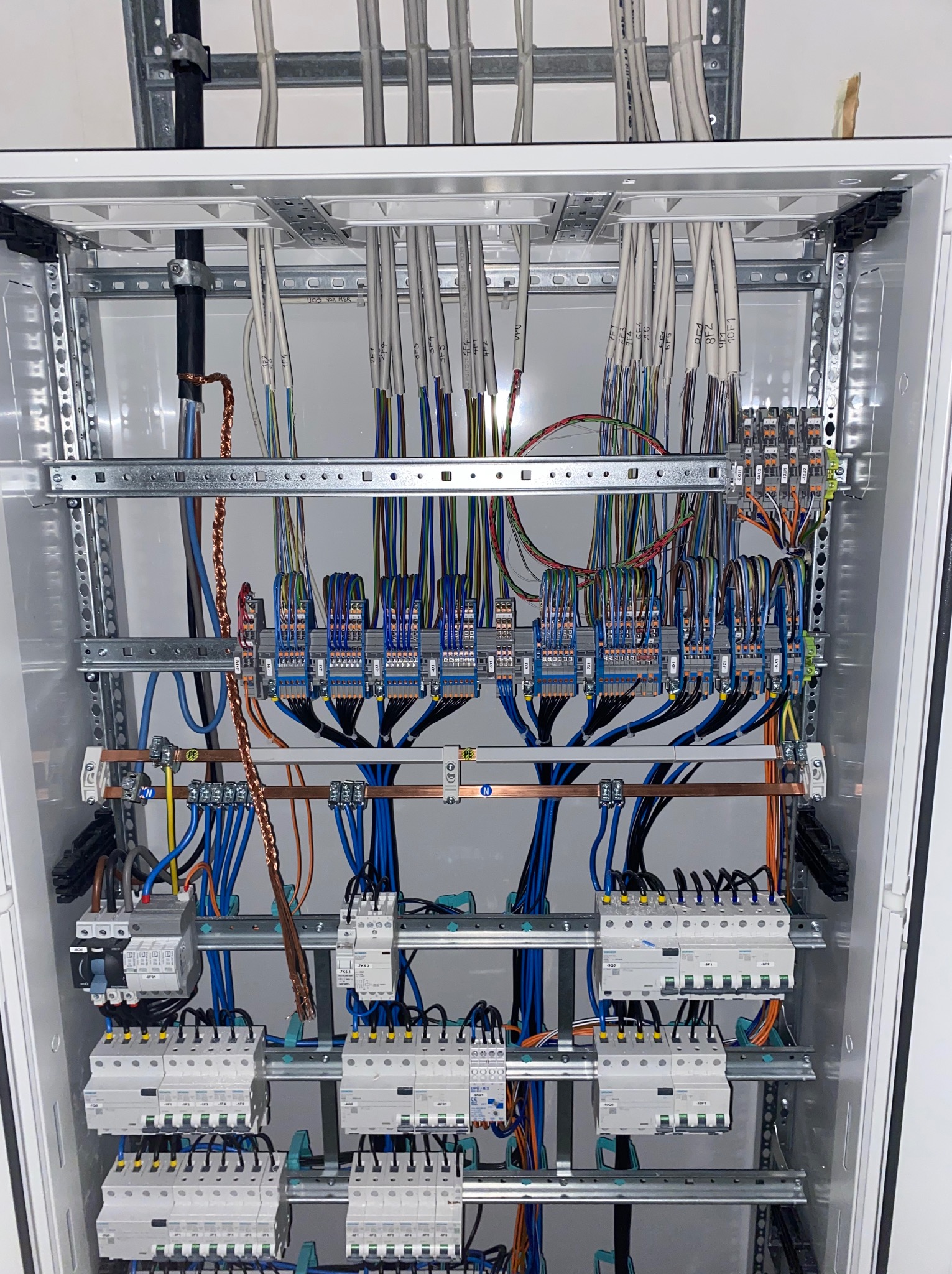 Szczegółowe ujęcie skrzynki elektrycznej z precyzyjnie ułożonymi przewodami i zabezpieczeniami, gotowej do działania. Widoczne oznaczenia na kablach.