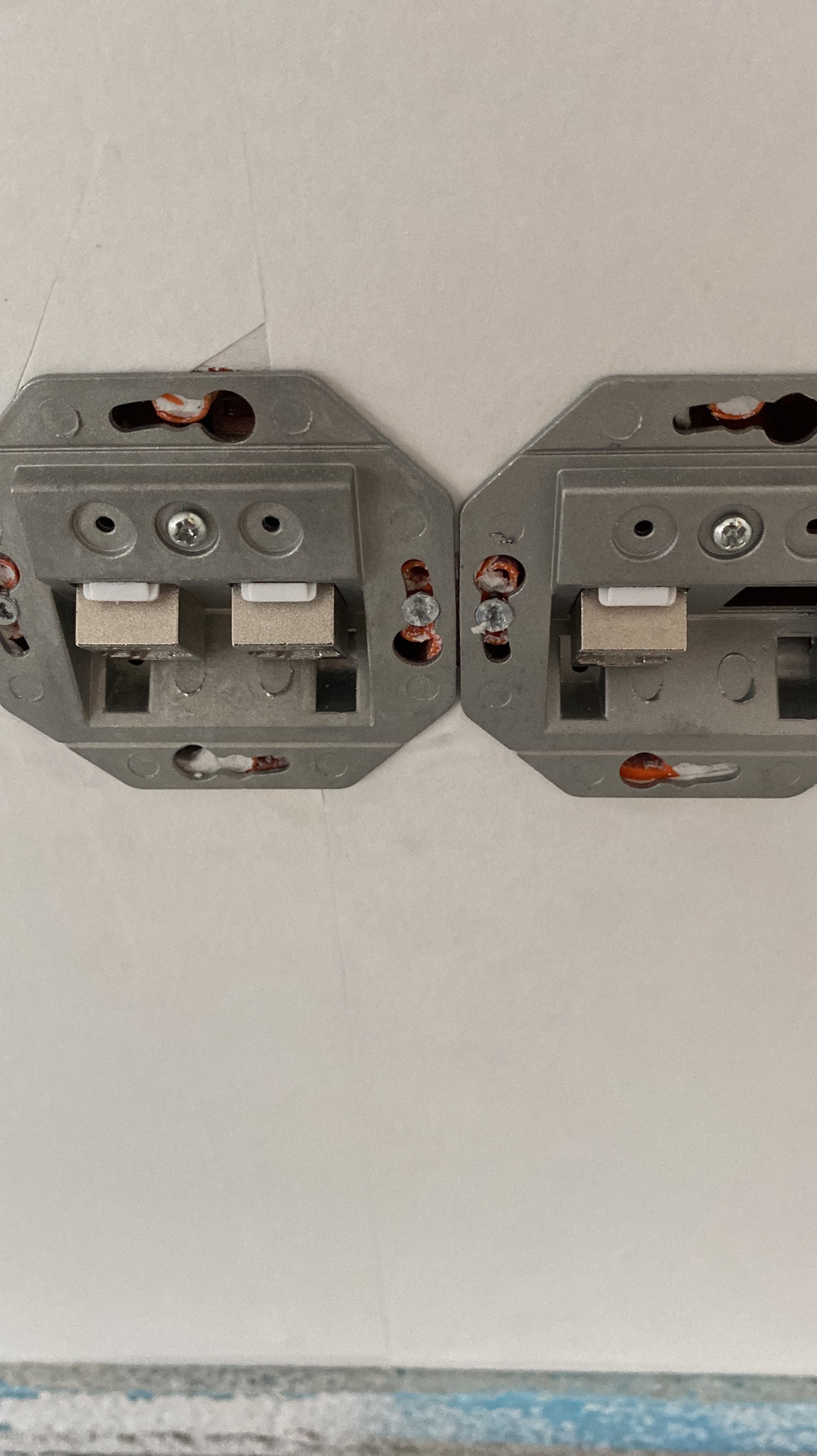 Dwa metalowe uchwyty oświetleniowe przymocowane do sufitu, widoczne przewody w otworach montażowych. Bliski plan, neutralne oświetlenie.