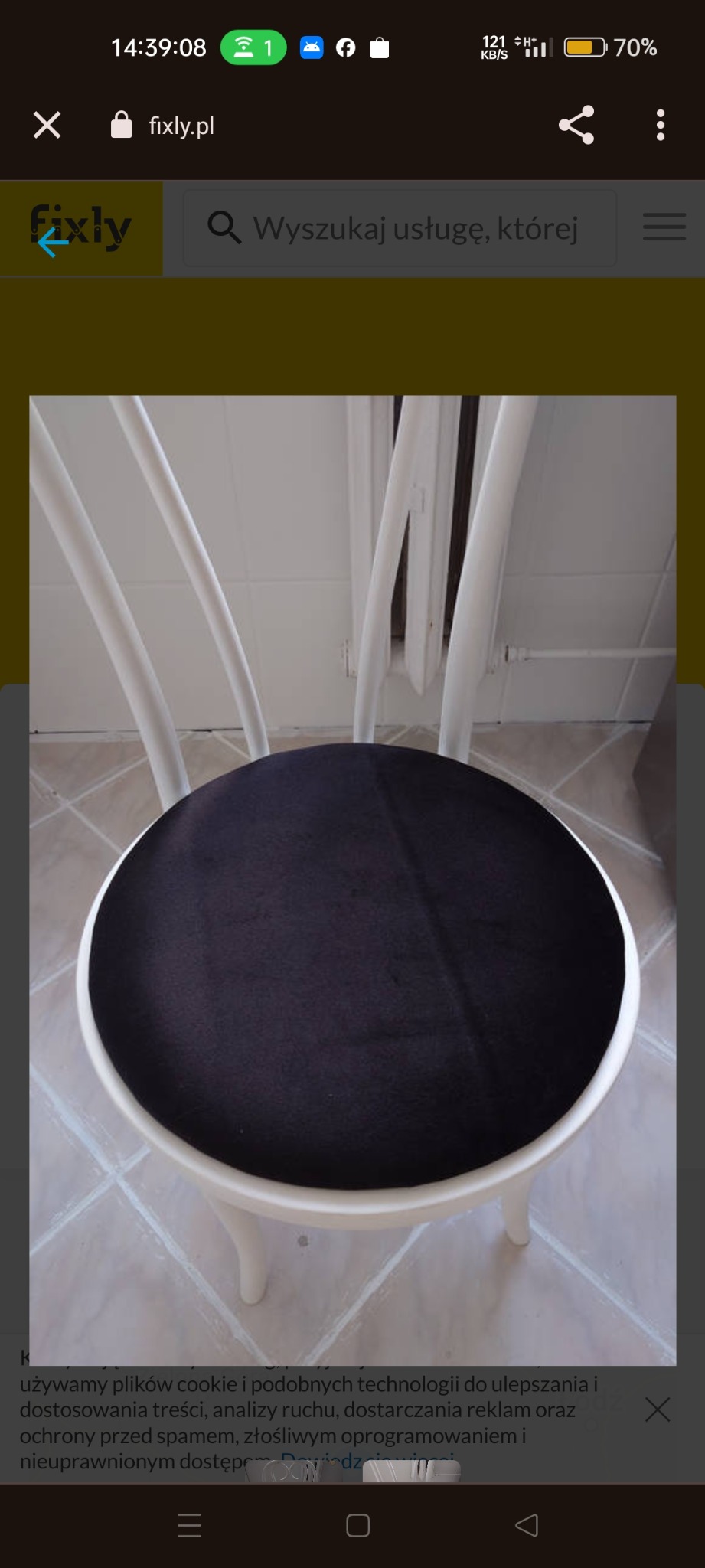 Krzesło po renowacji tapicerskiej z ciemnym, okrągłym siedziskiem na tle białych nóg i oparcia. Widoczny fragment podłogi z jasnych płytek.