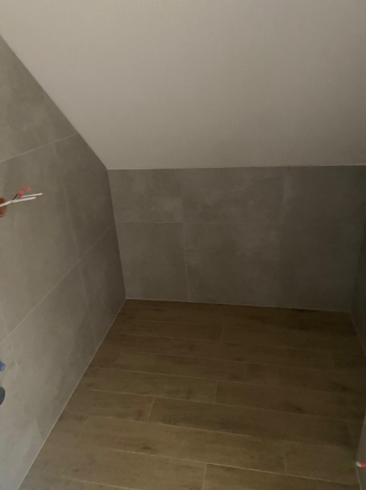 Ukończona łazienka na poddaszu z szarymi płytkami ściennymi i drewnopodobną podłogą. Uwagę przyciąga nietypowy kształt pomieszczenia.