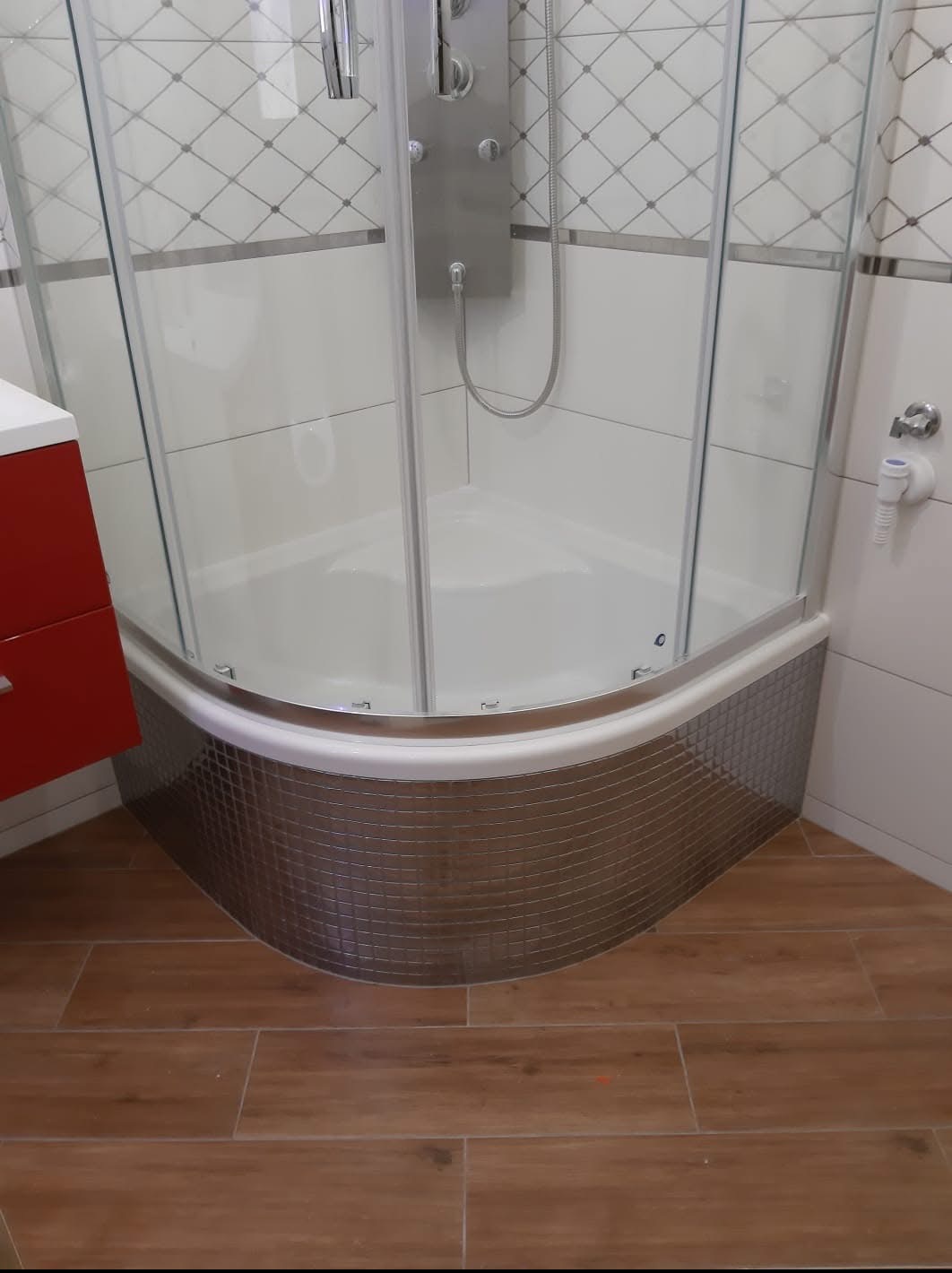 Nowoczesna kabina prysznicowa z hydromasażem, wykończona mozaiką i białymi płytkami z dekoracyjnym wzorem, na podłodze drewnopodobne płytki.