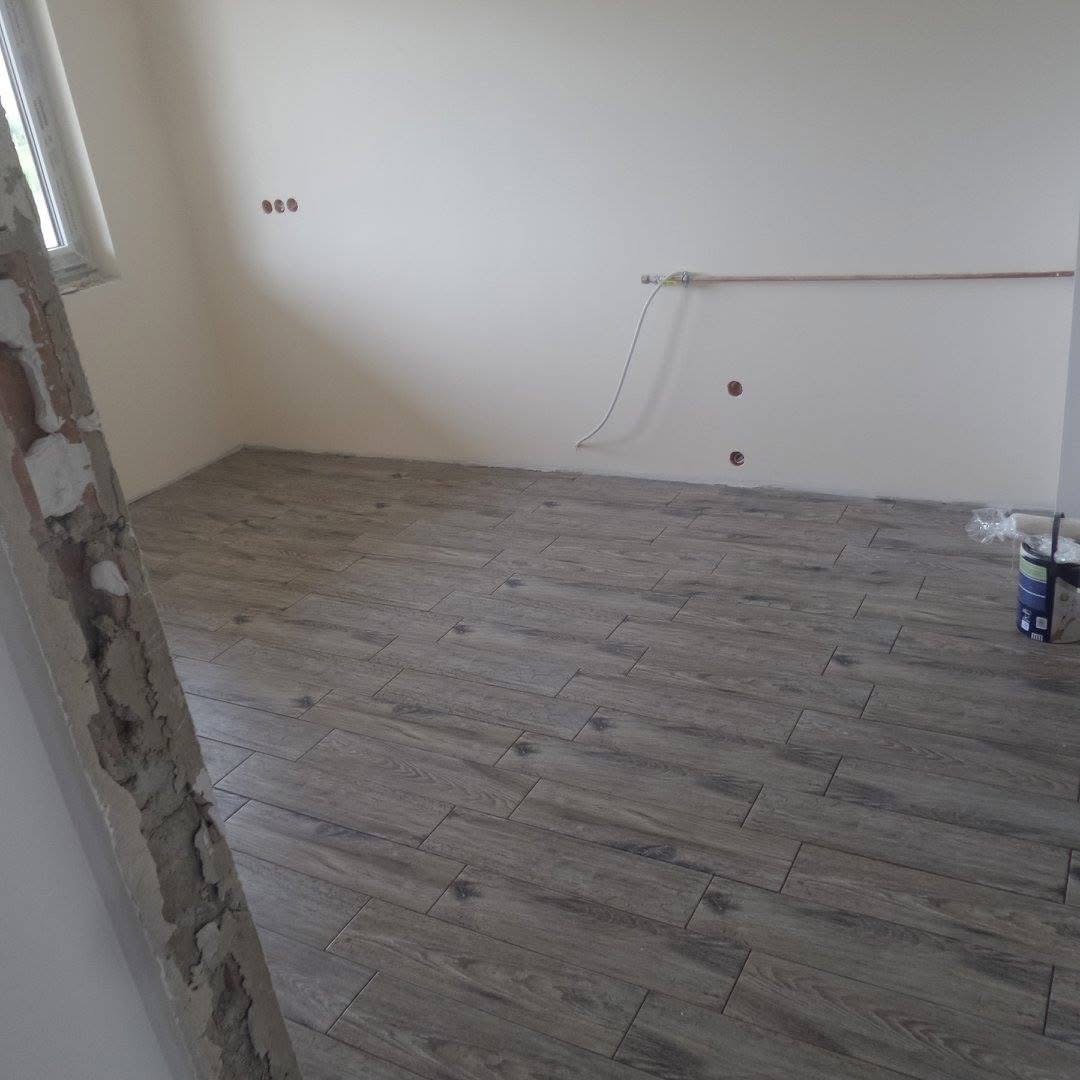 Ułożone płytki podłogowe imitujące drewno w pomieszczeniu w trakcie remontu. Fragment ściany z widocznymi instalacjami i niedokończonym wykończeniem.