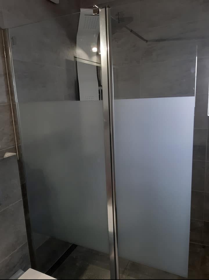 Nowoczesna kabina prysznicowa z matowymi szybami i chromowanymi profilami. Minimalistyczny design w szarej łazience. Widoczna deszczownica.