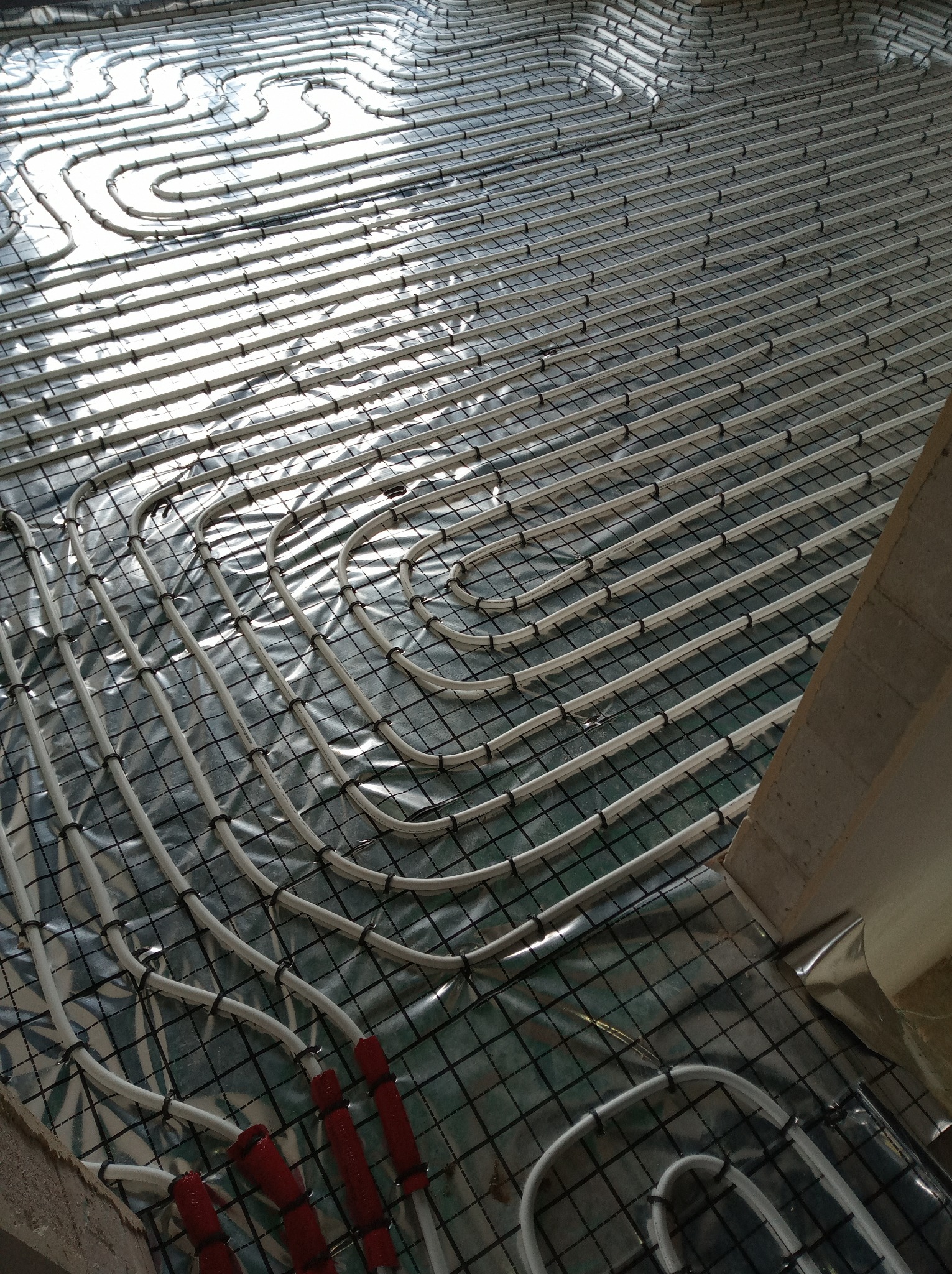 Ułożone rury w systemie  na folii z rastrem, przygotowane do wylania posadzki. Widoczne mocowania rur i fragment ściany.