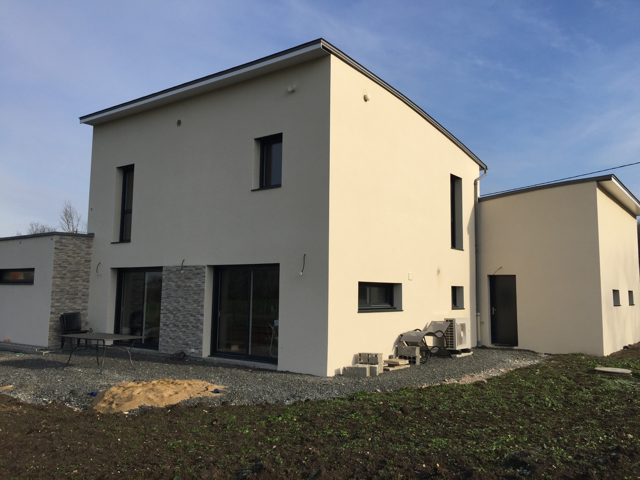 Nowoczesny, dwukondygnacyjny dom z jasną elewacją i grafitowymi oknami. Widoczny fragment tarasu z meblami i świeżo posadzona trawa. Minimalistyczny design.