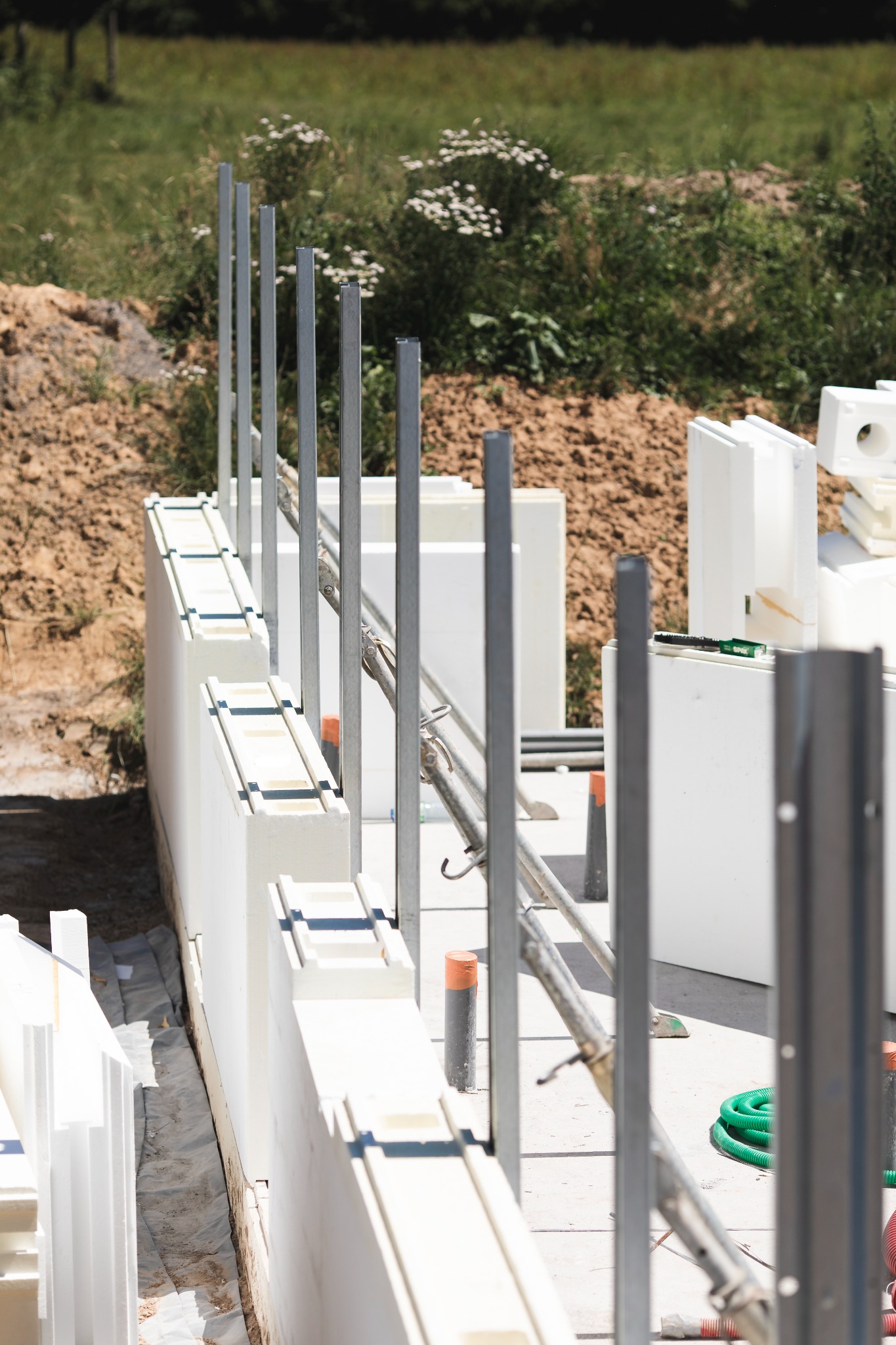 Budowa domu modułowego we Wrocławiu: białe ściany z izolacją, stalowe wzmocnienia i zielony wąż na placu budowy. Widok z góry na fundamenty.