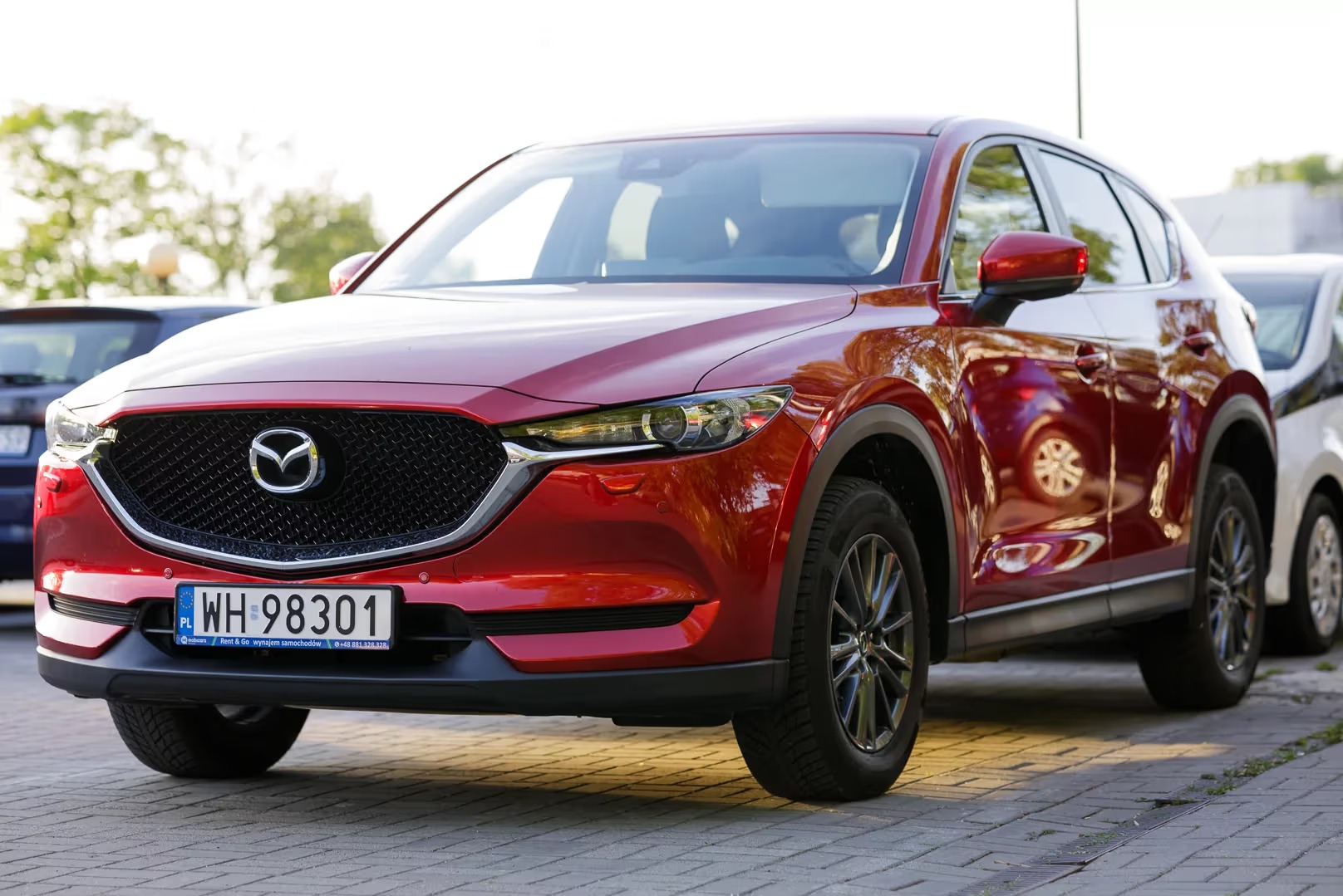 Czerwona Mazda CX-5 na wynajem, automat, widok z przodu, tablica rejestracyjna WH 98301, MobiCars, opony zimowe, lekko z boku, zaparkowana na kostce.