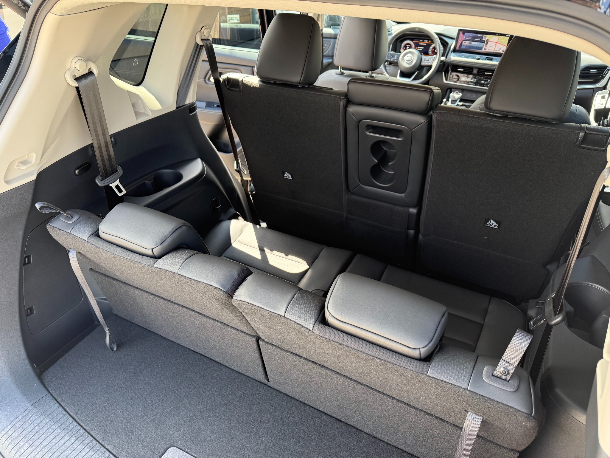 Wnętrze bagażnika 7-osobowego Nissana X-Trail z rozłożonymi fotelami trzeciego rzędu, widok z tyłu, wnętrze w odcieniach szarości, widoczny kokpit kierowcy.