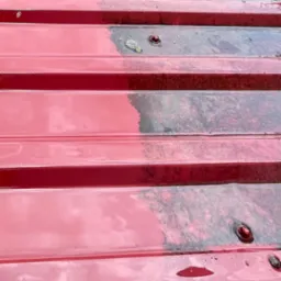 Czerwony dach z blachy trapezowej, częściowo umyty, ukazujący kontrast między czystą a zabrudzoną powierzchnią. Widoczne zacieki i drobne zabrudzenia.