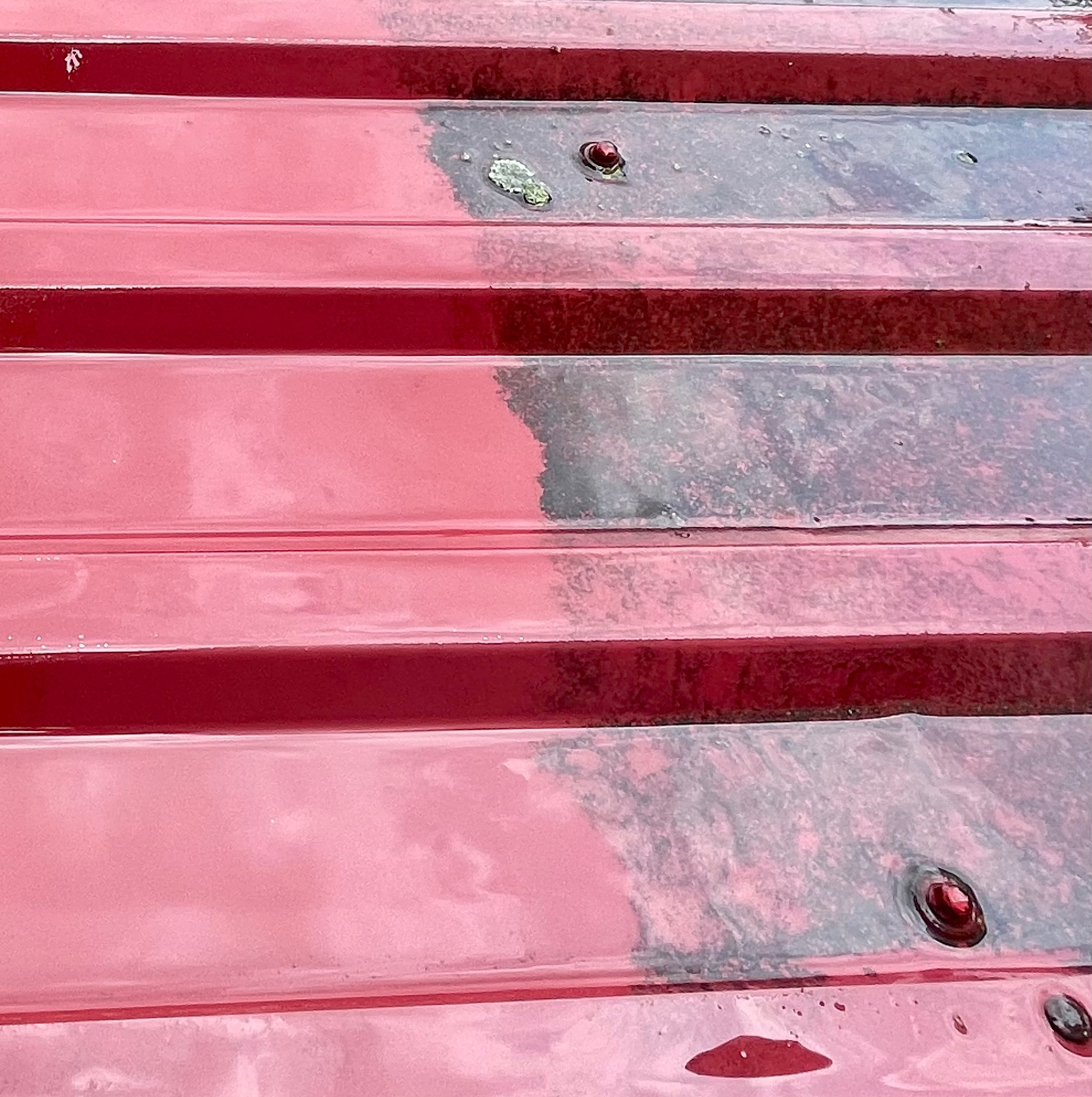 Czerwony dach z blachy trapezowej, częściowo umyty, ukazujący kontrast między czystą a zabrudzoną powierzchnią. Widoczne zacieki i drobne zabrudzenia.