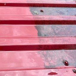 DS Dachbud - Daniel Sosiński - Częściowo wyczyszczony, czerwony dach z blachy trapezowej. Widoczna różnica między czystą a zabrudzoną powierzchnią. Krople wody na powierzchni.