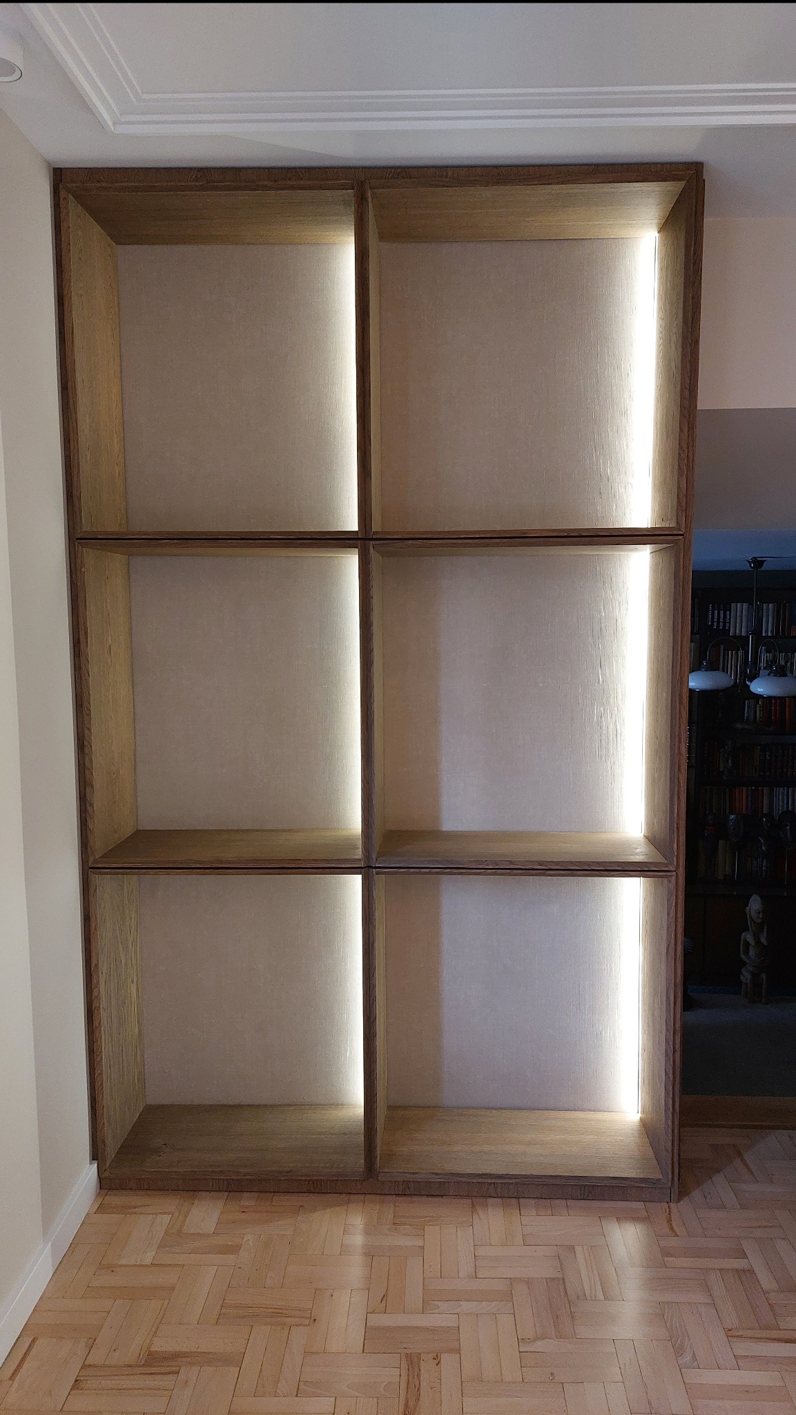 Drewniany regał z podświetleniem LED wbudowanym w przegrody, widok z dołu, parkiet na podłodze.