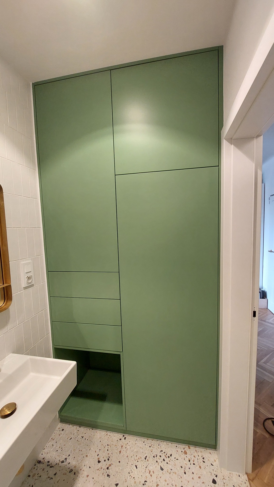 Zielona szafa łazienkowa na wymiar z szufladami i otwartą półką, dopasowana do wnętrza z umywalką i mozaikową podłogą. Minimalistyczny design, gładkie fronty.