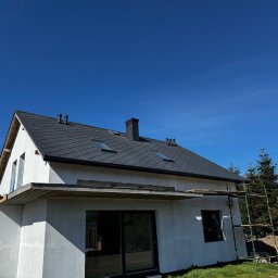 OL-DACH DEKARSTWO - Nowoczesny dom jednorodzinny z ciemną dachówką i oknami dachowymi, częściowo otynkowany, z widocznymi rusztowaniami i błękitnym niebem w tle.