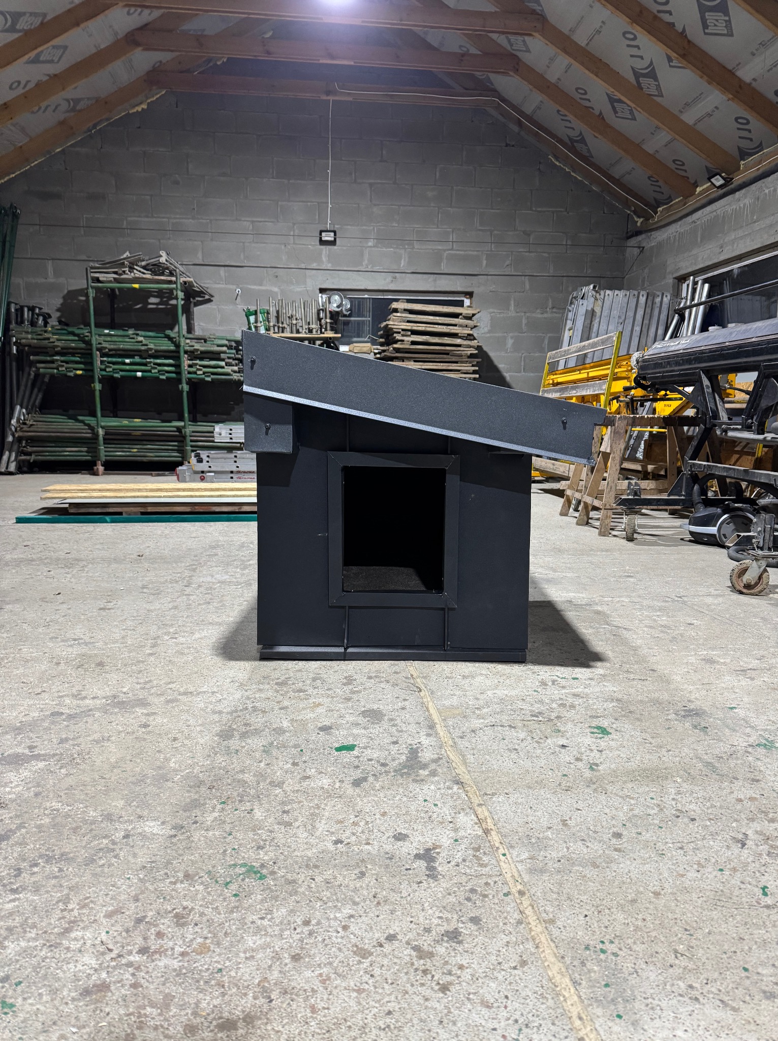 Nowoczesna obróbka blacharska w Ustarbowie. Czarna, metalowa konstrukcja z ukośnym dachem, widoczna na tle hali z materiałami budowlanymi. Precyzyjne wykonanie.