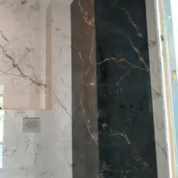 Wykończona ściana w łazience z marmurowymi płytkami w odcieniach bieli i czerni, z widoczną instalacją sanitarną i włącznikiem. Detal wykończenia wnętrza.