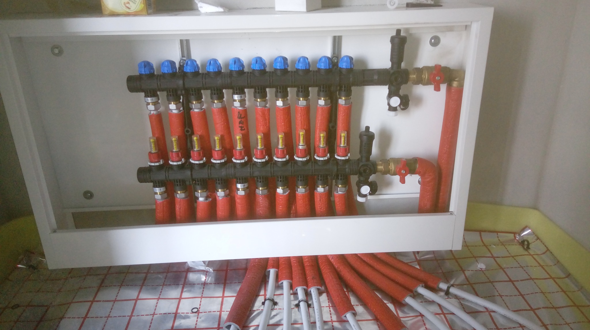 Rozdzielacz ogrzewania podłogowego z rurami w izolacji, zamontowany w szafce, widok z góry. Usługa wykonana w Przemyślu.