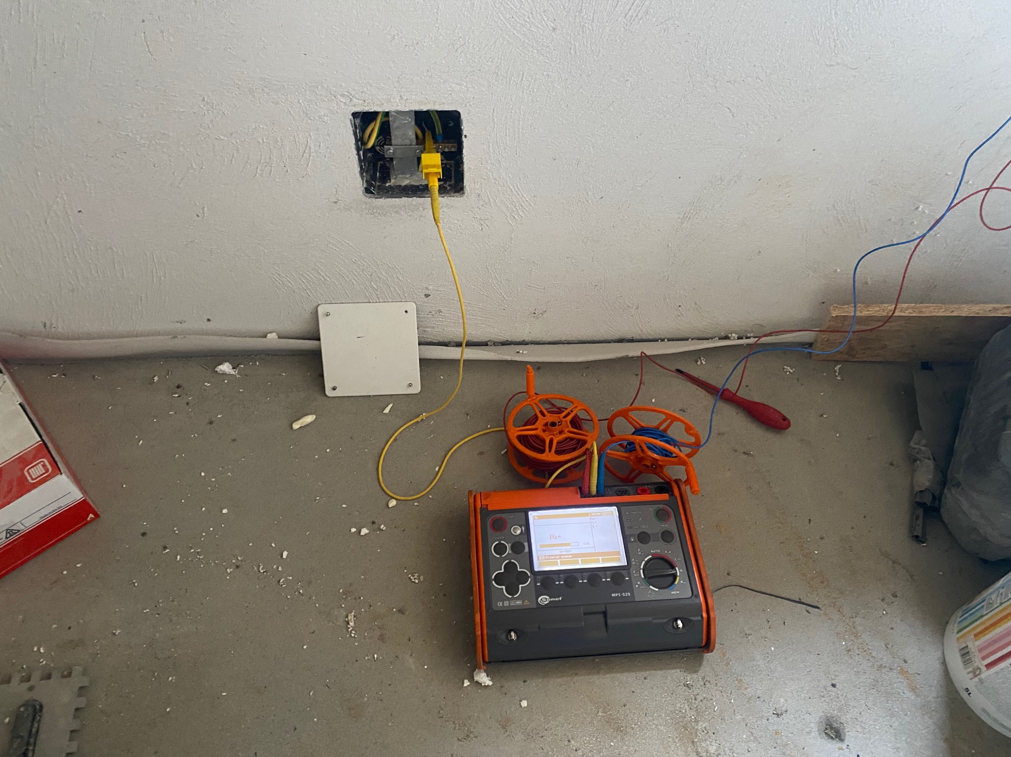 Miernik elektryczny Sonel MPI-525 podłączony do gniazdka w ścianie, obok narzędzia i przewody. Etap pomiarów w instalacji elektrycznej w trakcie prac wykończeniowych.