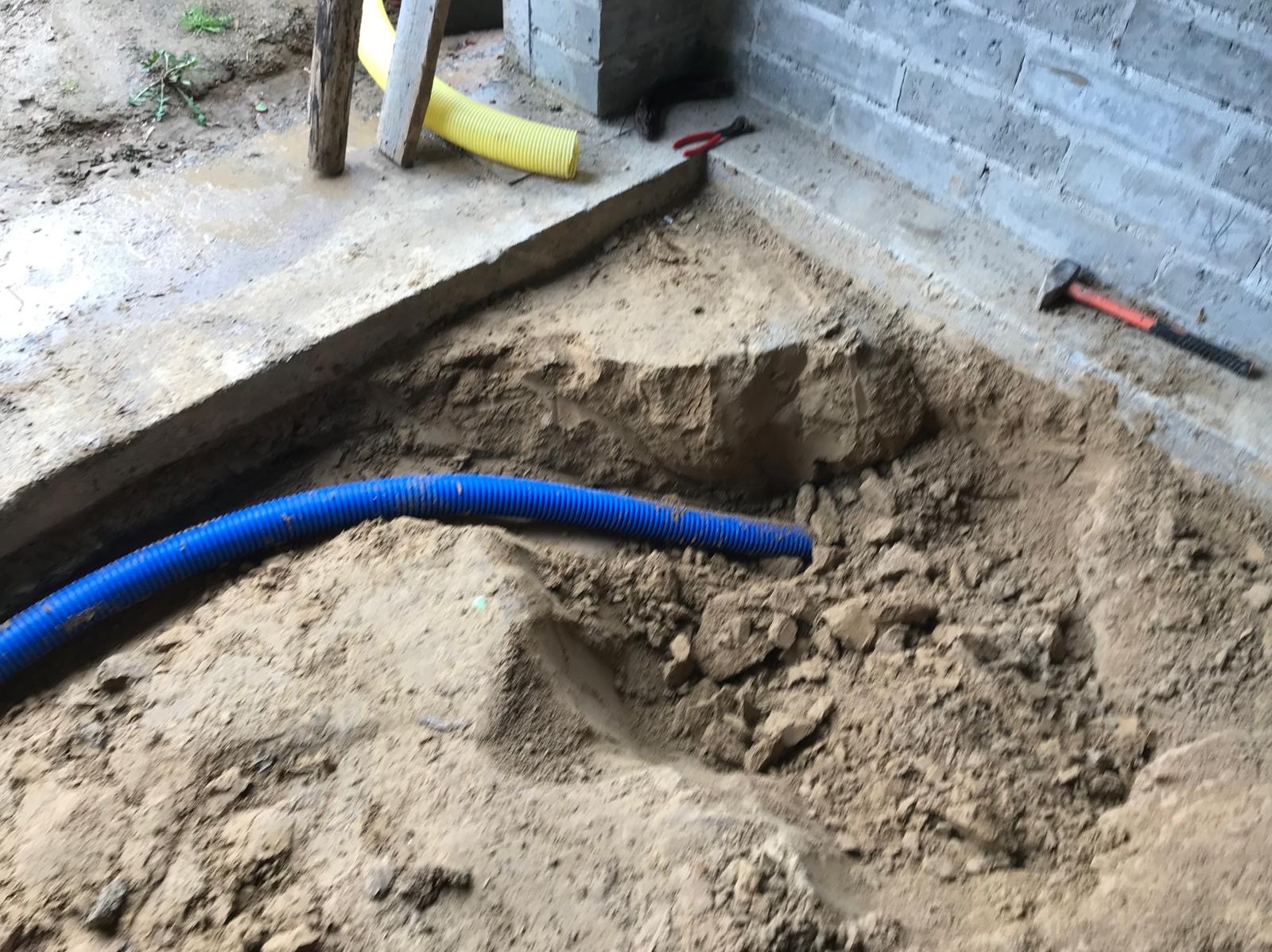 Niebieska rura karbowana w wykopie, żółta rura i narzędzia na betonowej powierzchni. Przygotowanie pod instalacje.