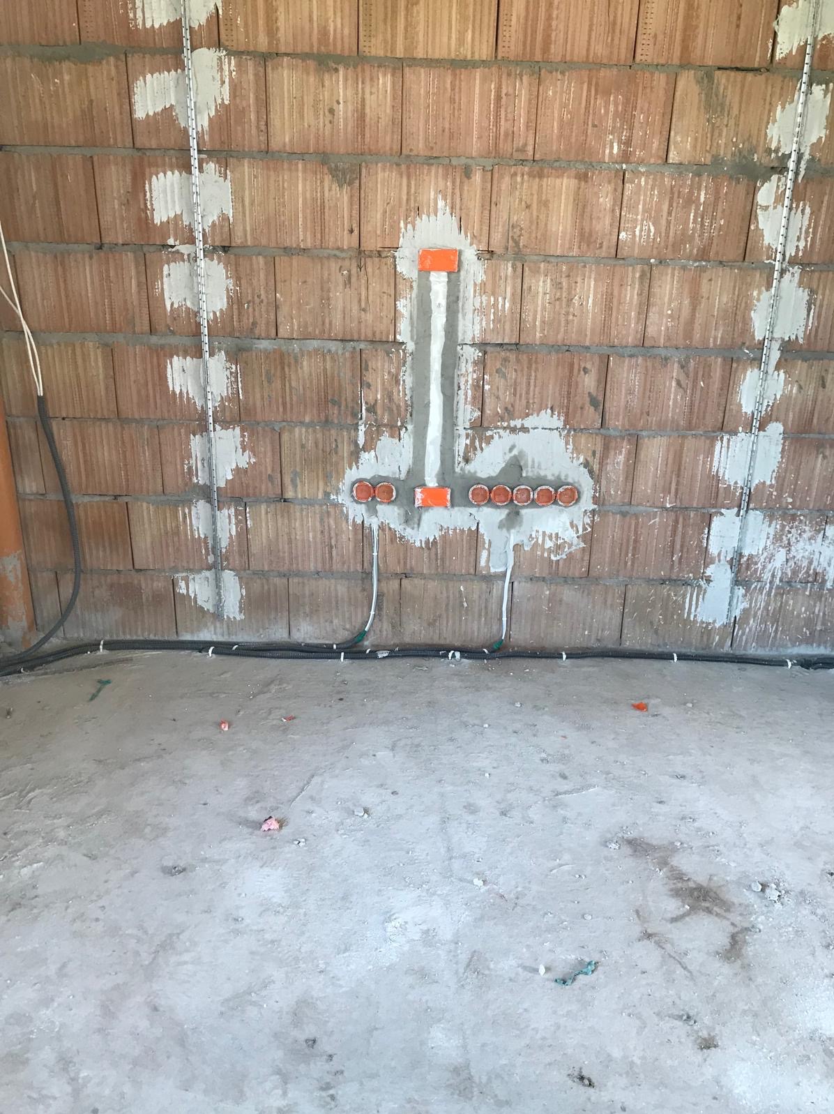 Instalacja elektryczna w trakcie montażu: puszki podtynkowe, przewody w peszlach, listwy montażowe na ceglanej ścianie. Widok na surowy stan.