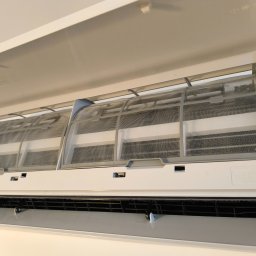 BessCool Klimatyzacja - Otwarty, biały klimatyzator z widocznymi, zakurzonymi filtrami siatkowymi. Widoczne żebra chłodzące i obudowa z napisem 'Manual/Auto'.