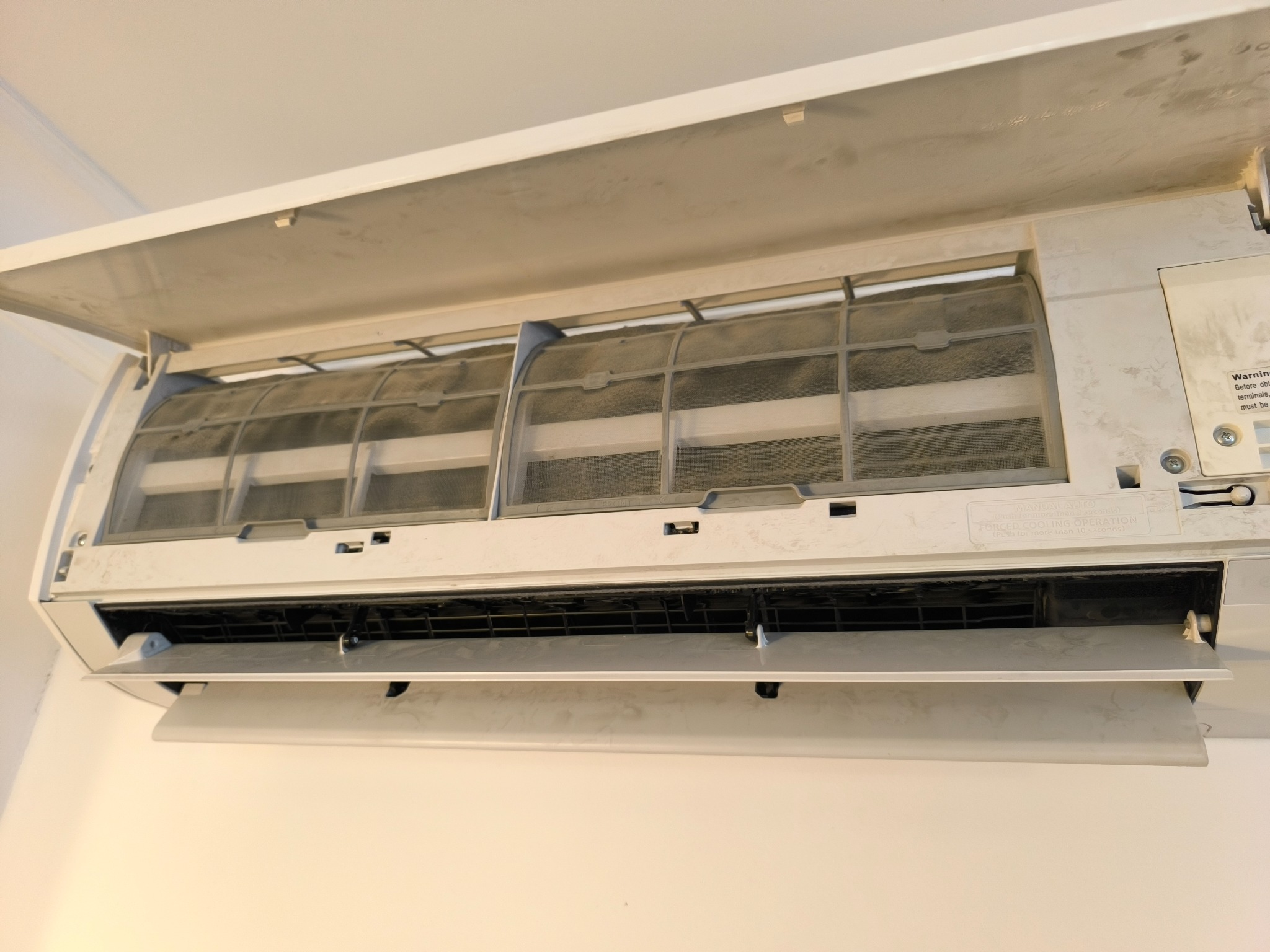 Otwarty klimatyzator ścienny z widocznymi, zakurzonymi filtrami. Widoczne ślady zabrudzeń na obudowie, co sugeruje potrzebę serwisu i czyszczenia.