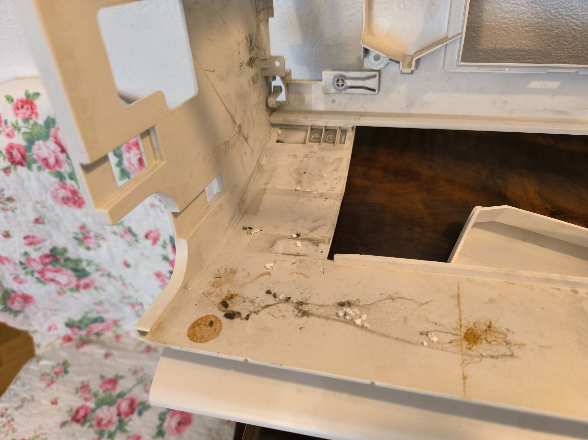Brudna, rozłożona obudowa klimatyzatora z widocznymi śladami pleśni i kurzu, leżąca na kwiecistej tkaninie. Widoczny drewniany blat w tle.