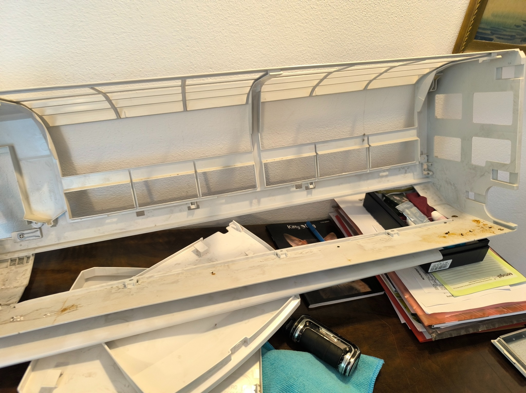 Brudna, rozmontowana obudowa klimatyzatora leży na stole, ukazując potrzebę czyszczenia i konserwacji. Widoczne ślady użytkowania i nagromadzony kurz.