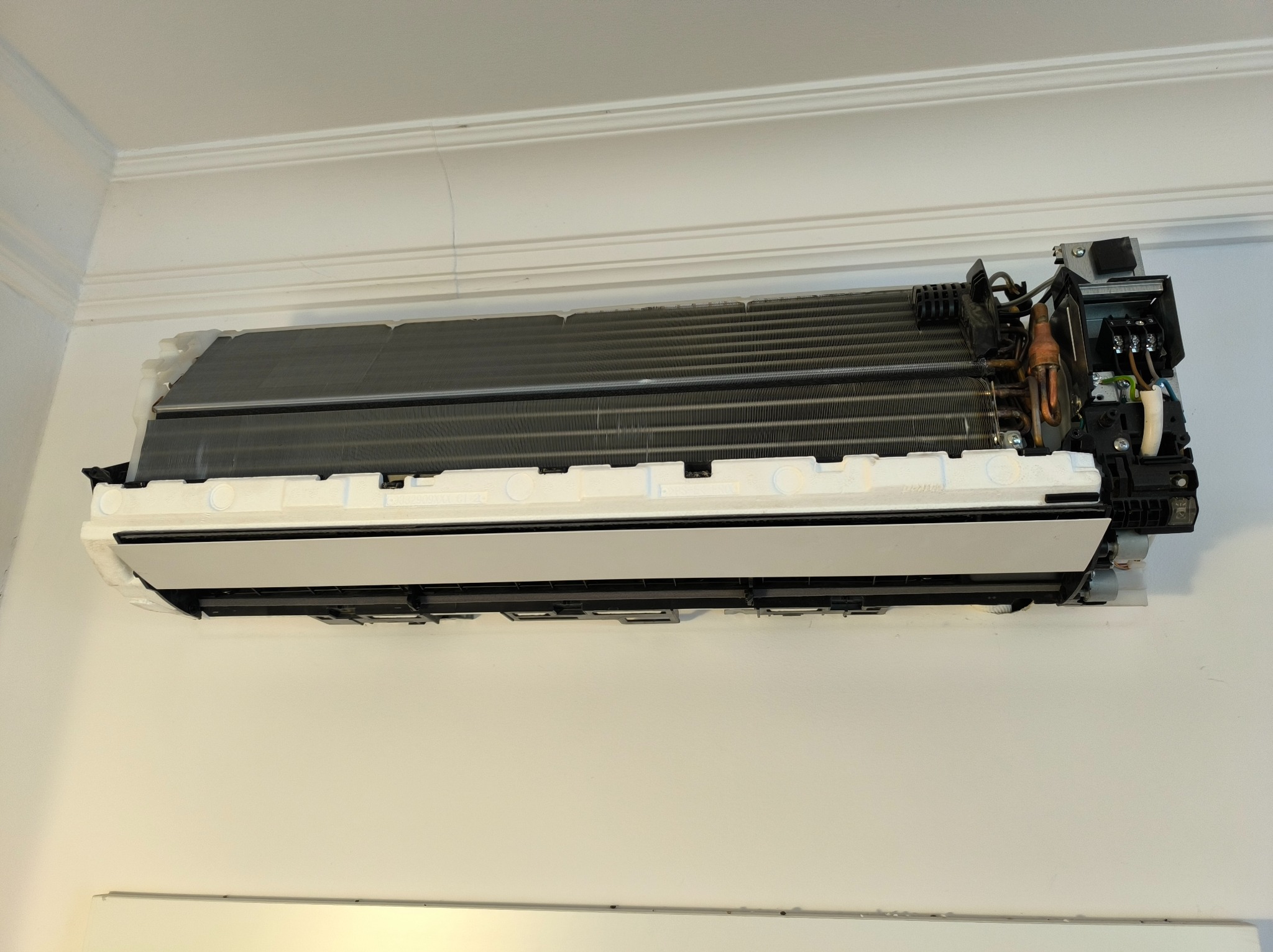 Rozłożona jednostka wewnętrzna klimatyzacji ściennej podczas serwisu. Widoczne filtry, elementy instalacji elektrycznej i rurki miedziane. Białe ściany i sufit w tle.