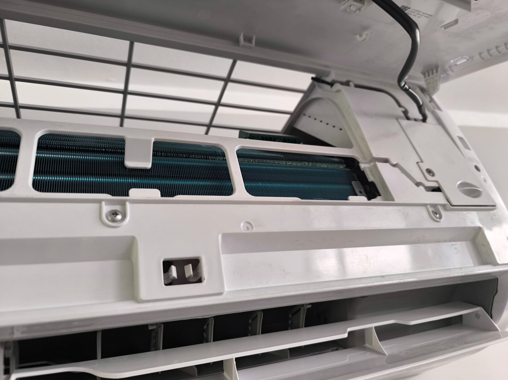 Wnętrze otwartej, białej klimatyzacji z widocznymi, chłodzącymi, niebieskimi żebrami, w trakcie czyszczenia lub serwisu. Widoczne śruby i elementy montażowe.