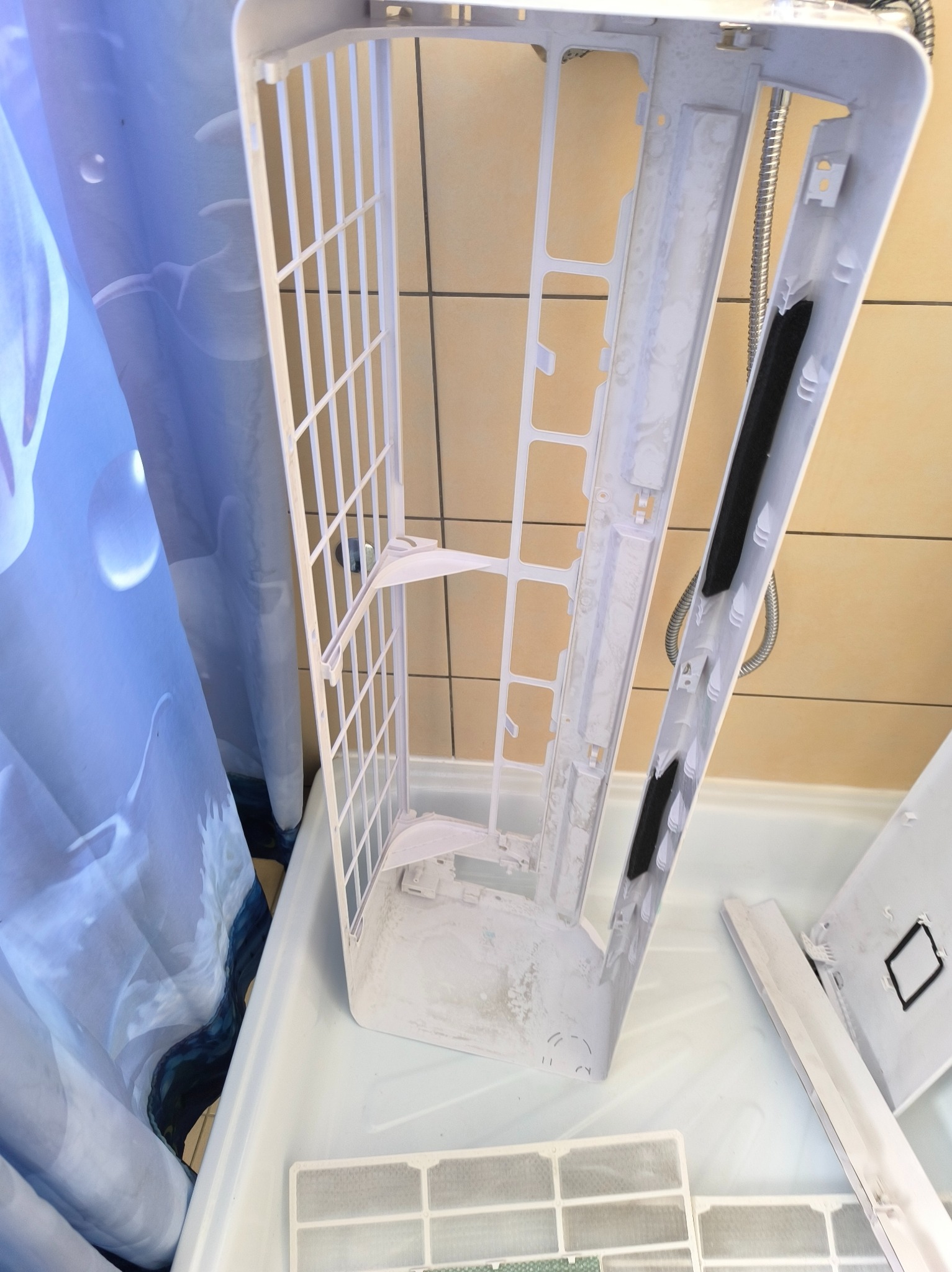 Czyszczenie klimatyzacji: rozłożone elementy jednostki wewnętrznej, widoczne filtry i obudowa w trakcie mycia, w tle kabina prysznicowa.