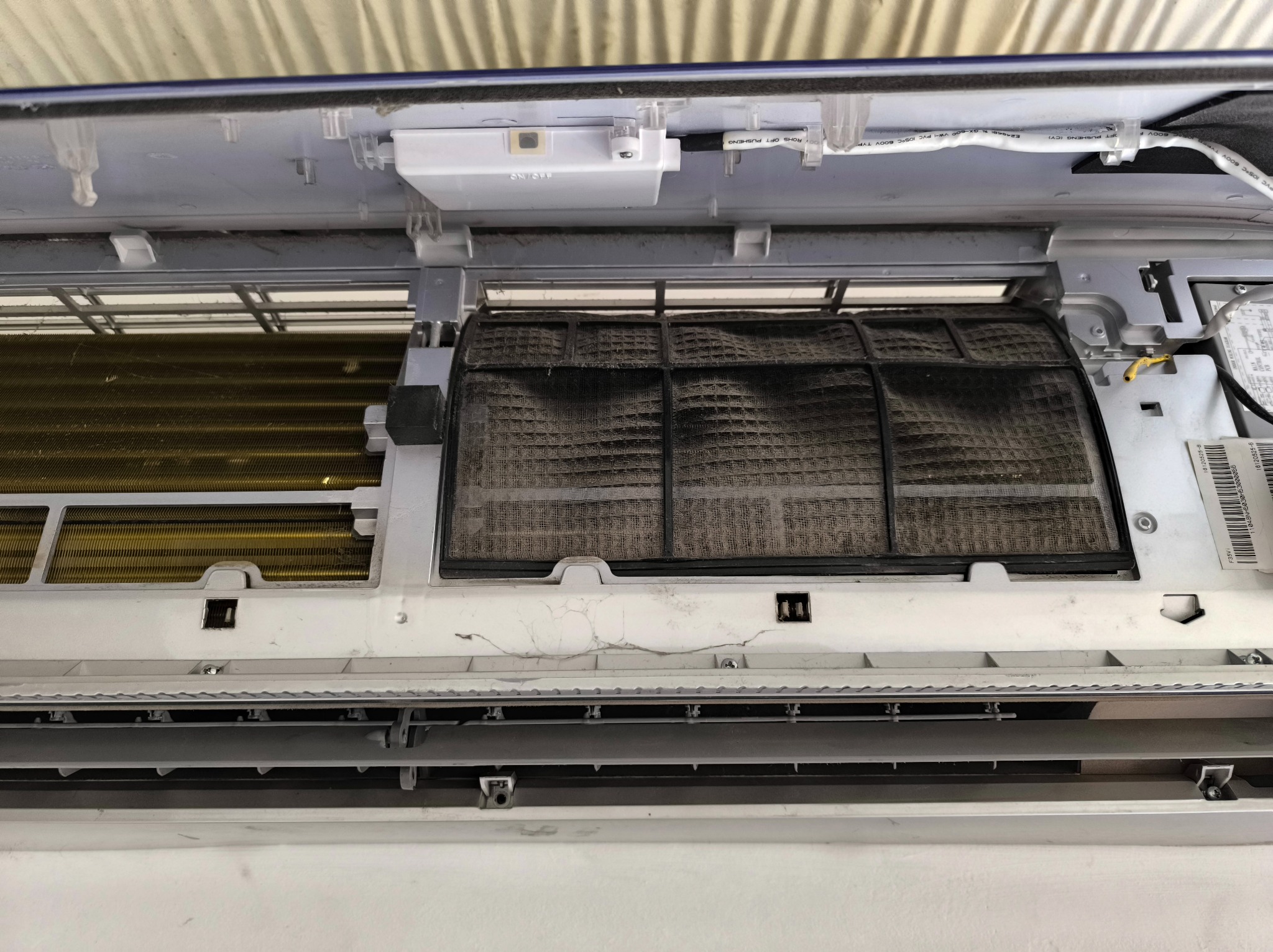 Otwarta obudowa klimatyzatora z bardzo brudnym filtrem, widoczne elementy wewnętrzne urządzenia przed czyszczeniem. Zaniedbany stan techniczny.