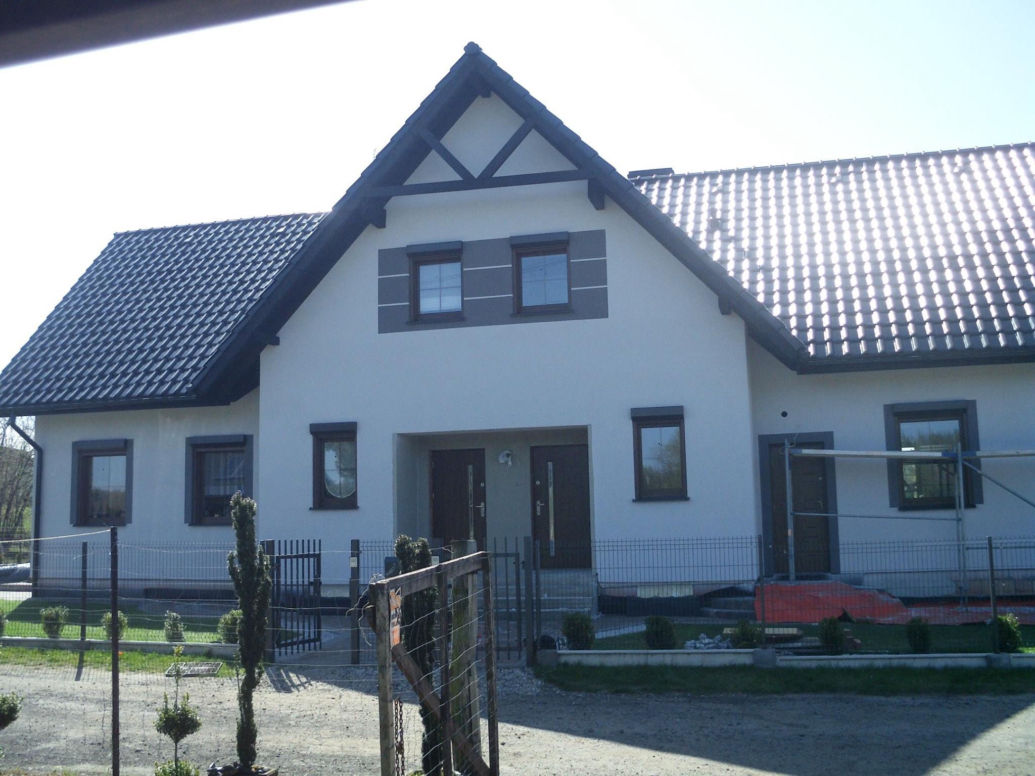 Elewacja odnowionego domu jednorodzinnego z ciemną dachówką i stolarką okienną. Widoczne rusztowanie sugeruje trwające prace wykończeniowe.
