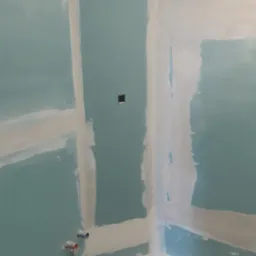 Ściany z płyt gipsowo-kartonowych po szpachlowaniu w Bolesławcu. Widoczne łączenia płyt, przygotowane do dalszych prac wykończeniowych. Instalacja wodna.