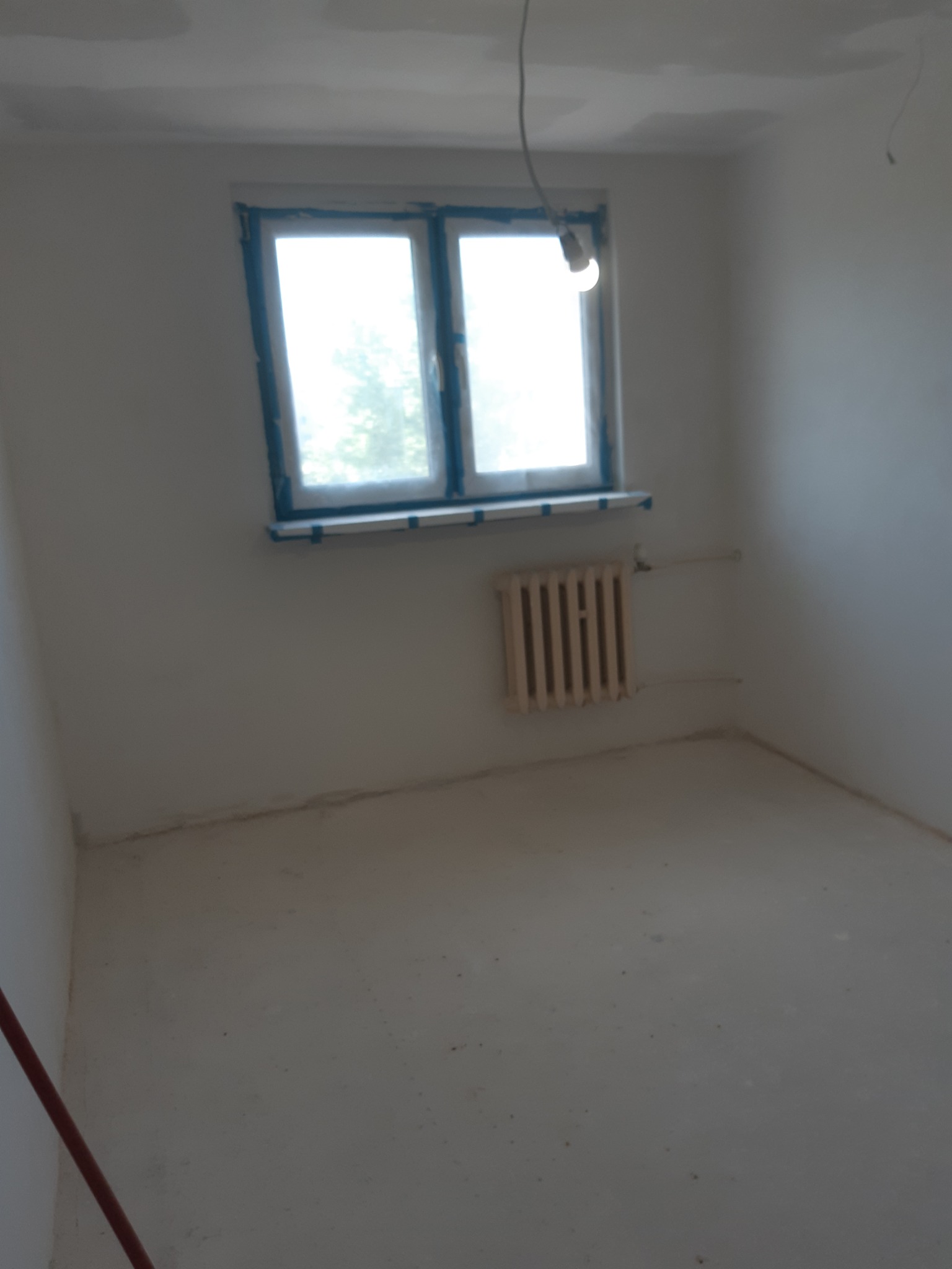 Pokój po szpachlowaniu ścian i sufitu, okno zabezpieczone folią, grzejnik. Przygotowanie do malowania.