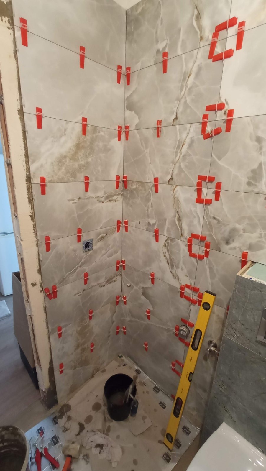 Układanie marmurowych płytek w łazience z użyciem poziomicy i czerwonych krzyżyków dystansowych, widoczny fragment instalacji.