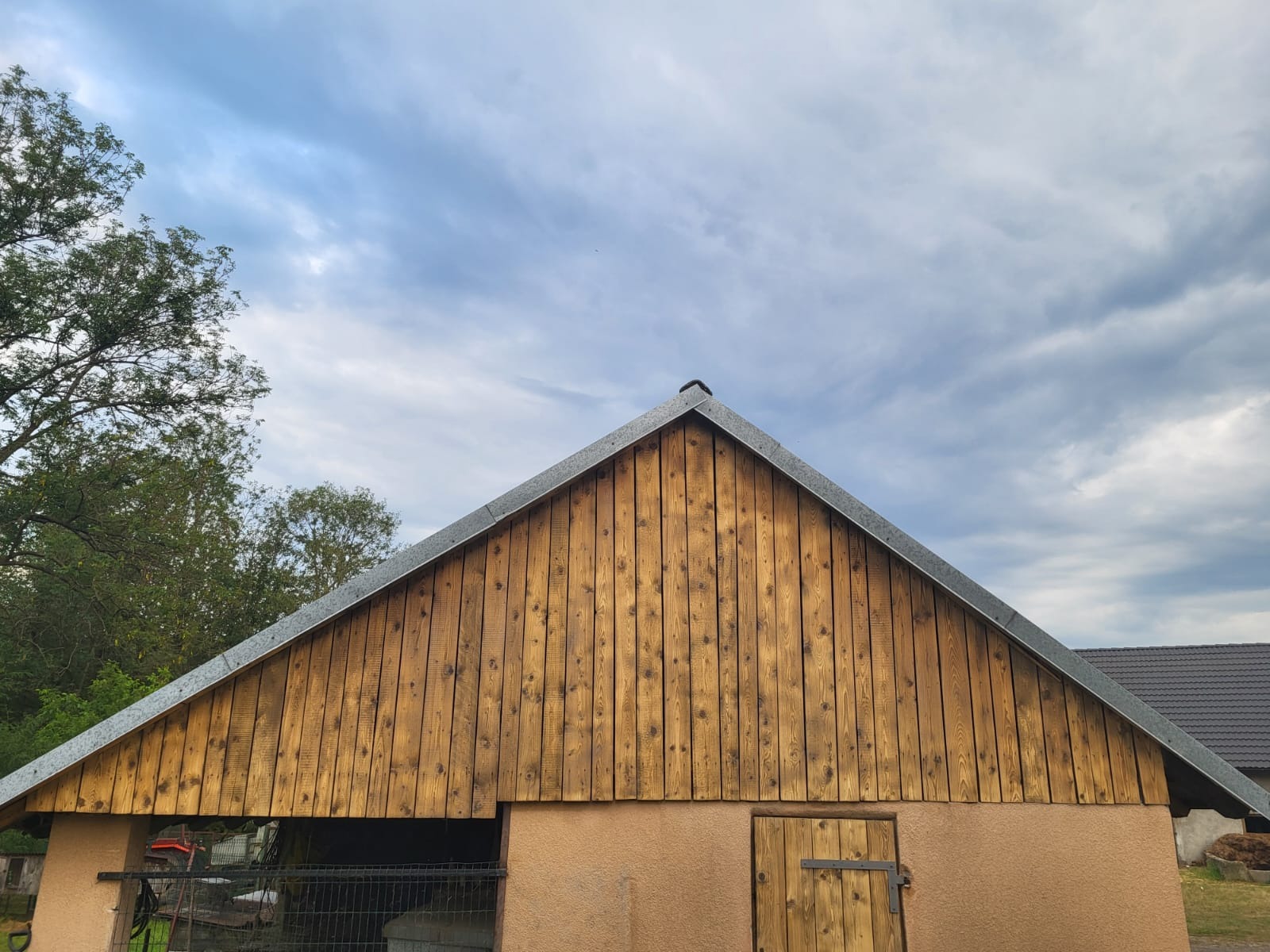 Odnowiona elewacja drewniana budynku gospodarczego po zabiegach czyszczących, z widocznymi detalami faktury drewna i metalowego okapu dachu. Ujęcie z dołu.