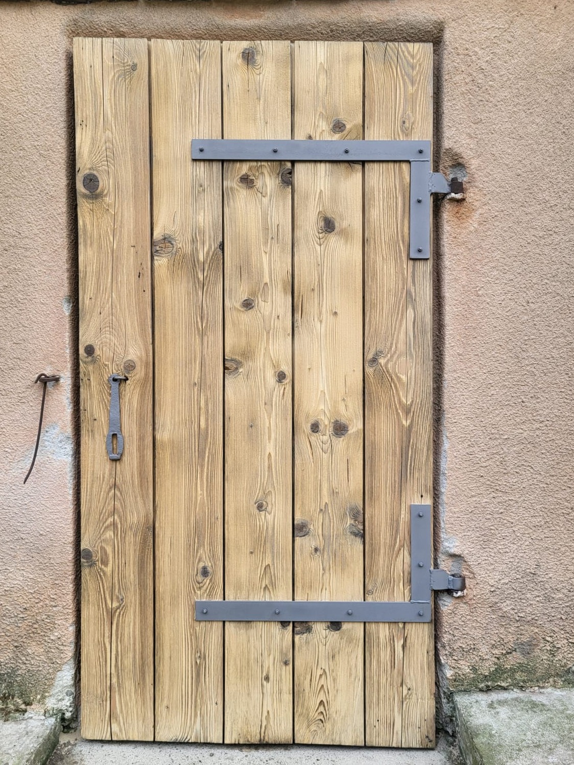 Drewniane drzwi z metalowymi okuciami, po procesie czyszczenia, ukazujące naturalną strukturę drewna i odświeżony wygląd. Widoczne ślady wcześniejszego użytkowania.