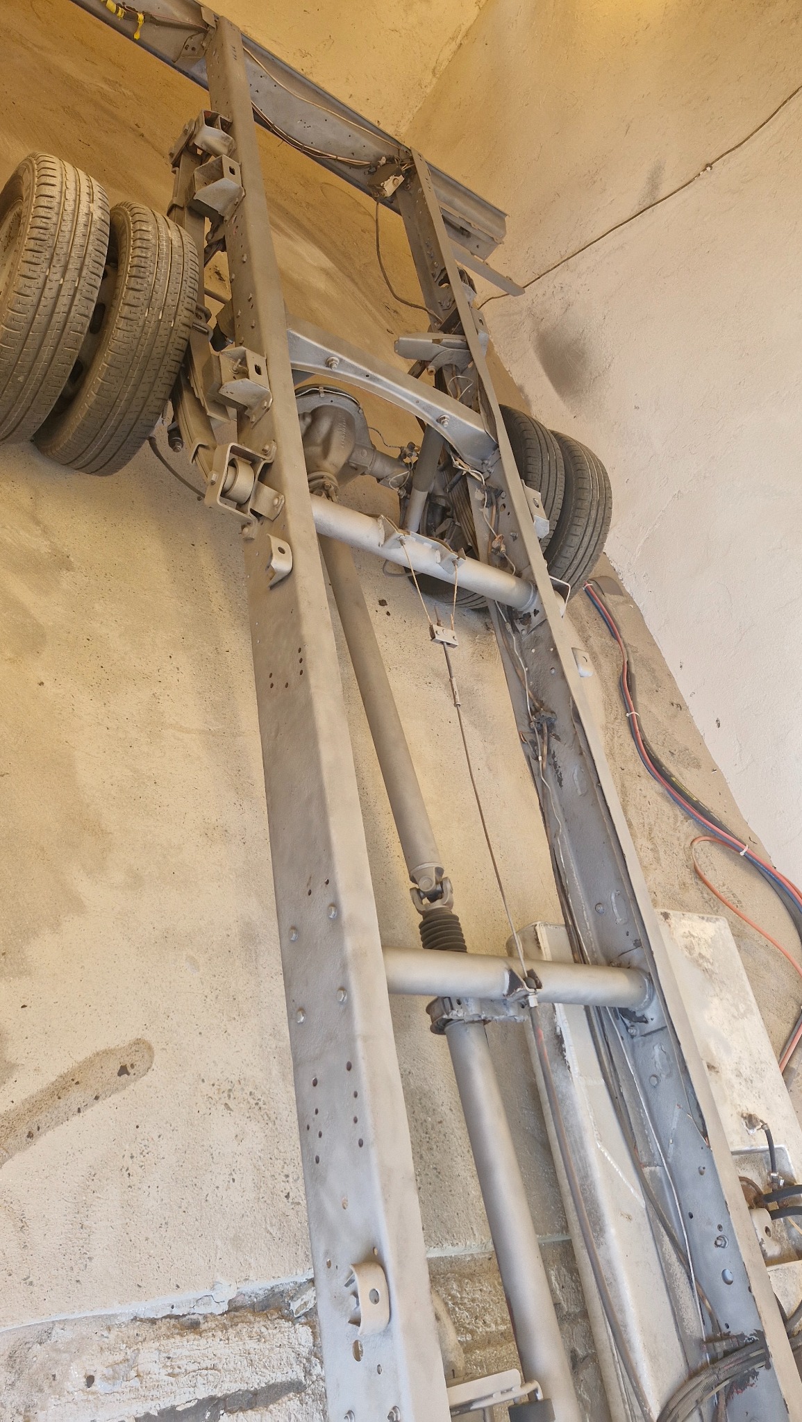 Oczyszczona rama pojazdu z kołami, po obróbce, w warsztacie. Widoczne elementy zawieszenia i układu napędowego. Szary, matowy kolor ramy.