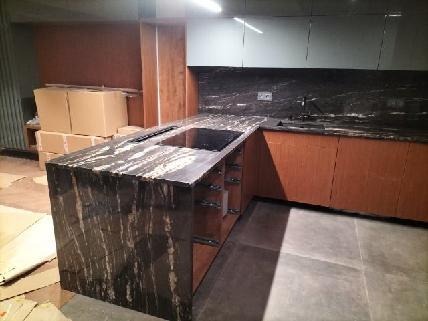 Kuchenny blat z kamienia o unikalnym wzorze żyłkowania, wkomponowany w nowoczesną zabudowę. Widoczne kartony w tle sugerują świeży montaż.