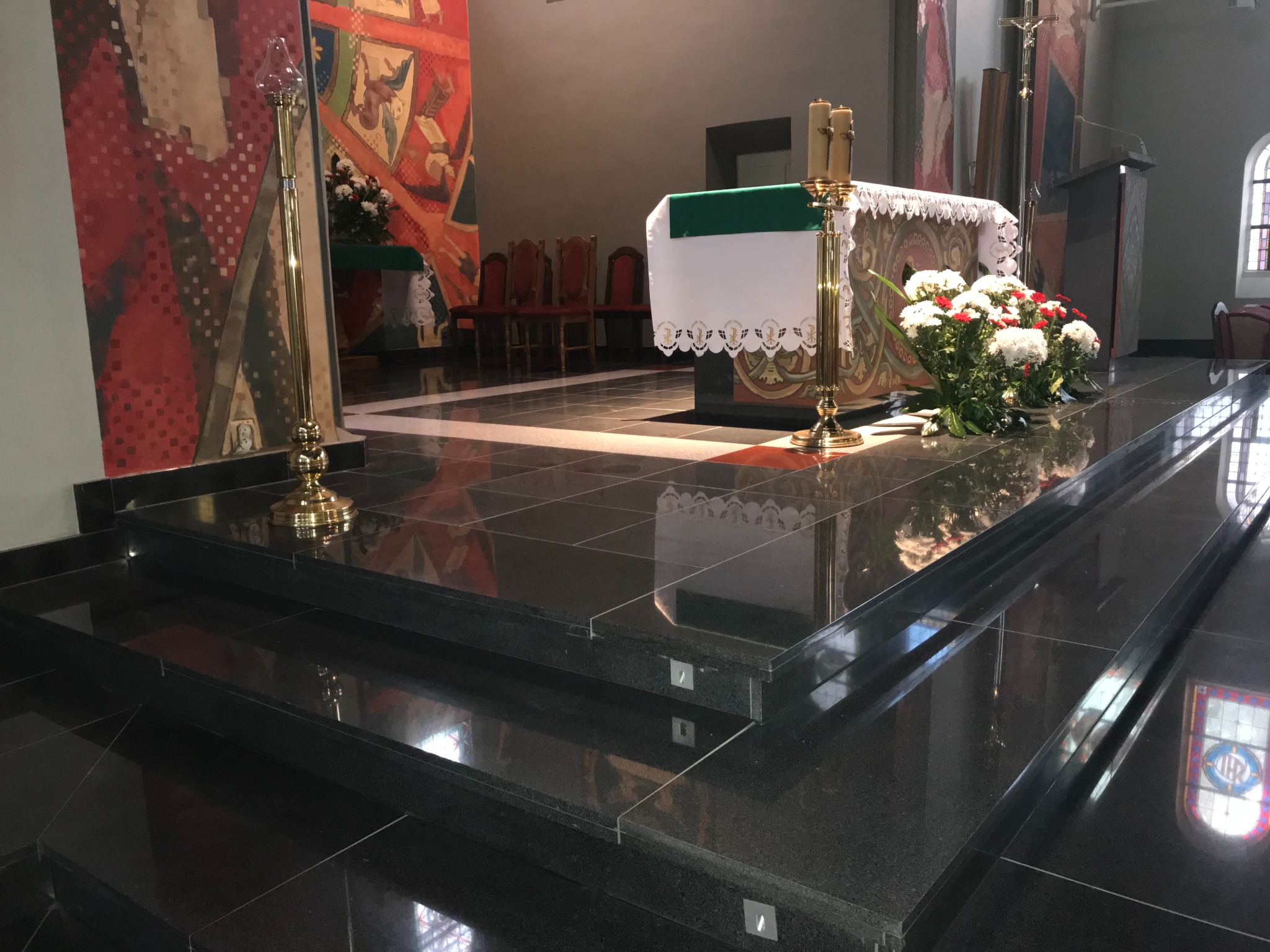 Polerowane, czarne schody kamienne prowadzą do ołtarza w kościele. Widoczne detale wykończenia i odbicia światła na gładkiej powierzchni.