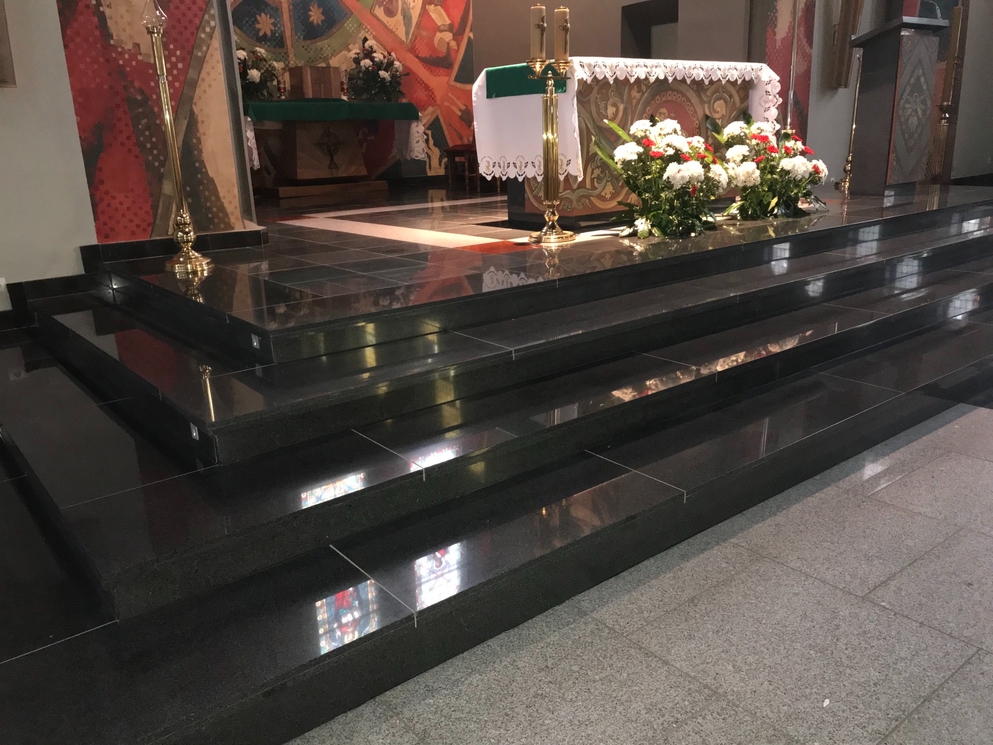Kamienne schody w kościele w Daleszycach. Polerowane, czarne płyty kamienne na stopniach odbijają światło, tworząc elegancki efekt. Widoczne elementy wystroju wnętrza.