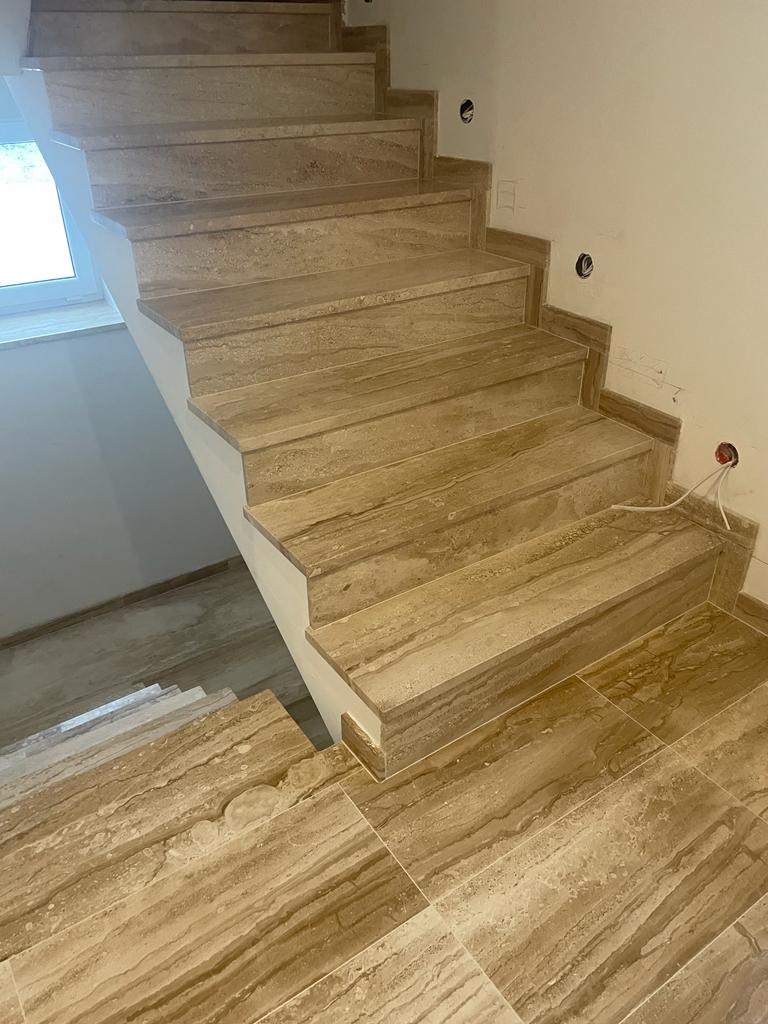 Wykończone schody kamienne wewnątrz budynku, z widocznymi stopniami i fragmentem podłogi, wszystko w beżowym odcieniu z charakterystycznym wzorem.