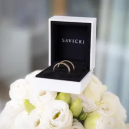Obrączki Savicki w białym pudełku na bukiecie białych róż. Delikatne światło, subtelne tło. Zdjęcie autorstwa @Trippujemy.
