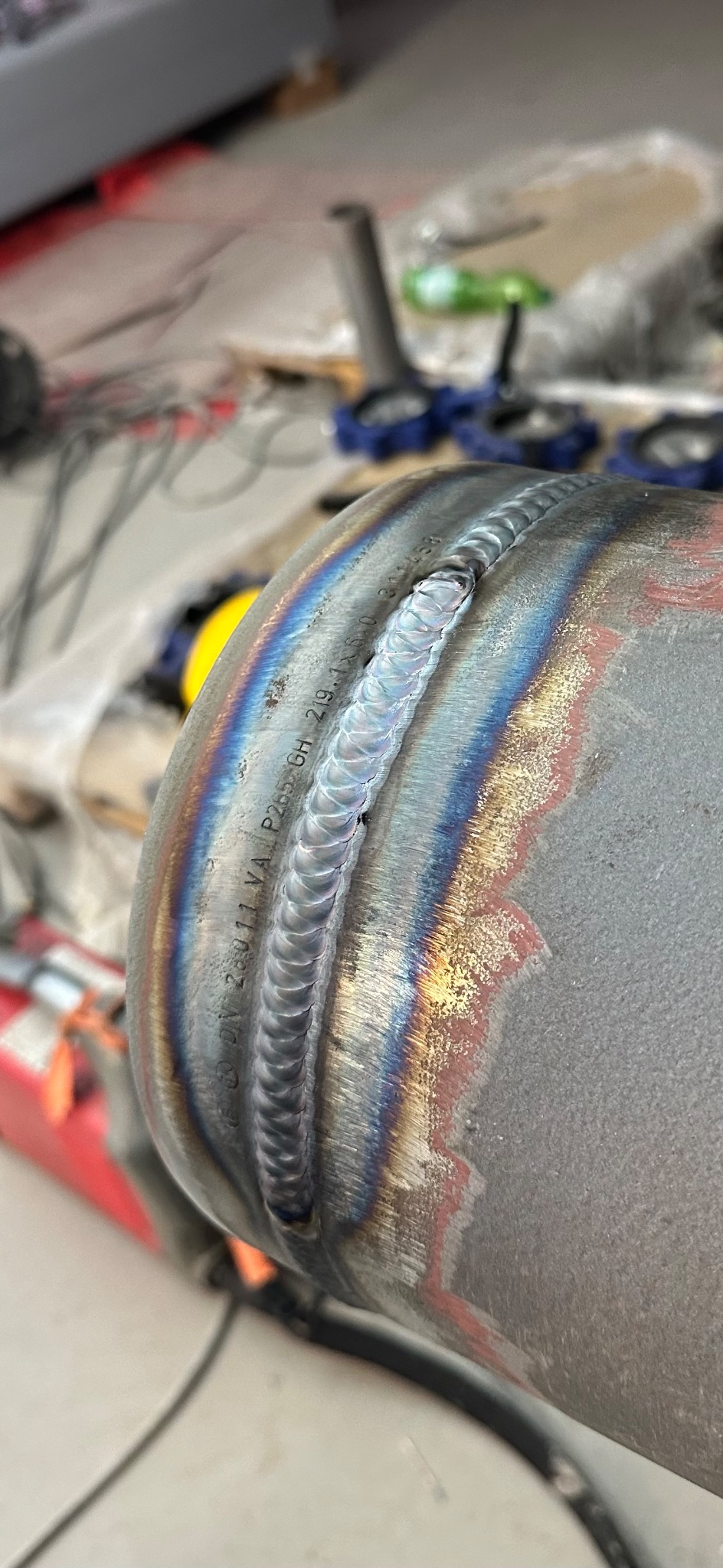 Precyzyjny spaw na metalowej rurze z widocznymi tęczowymi przebarwieniami termicznymi wzdłuż spoiny. Bliskie ujęcie, skupione na jakości wykonania.